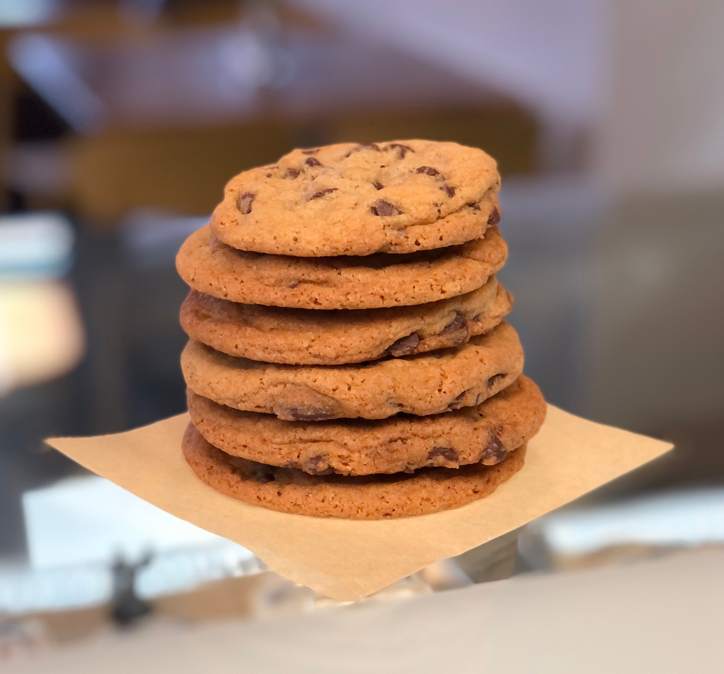 Stack of six chocolate chip cookies on a piece of paper, with a blurred background.