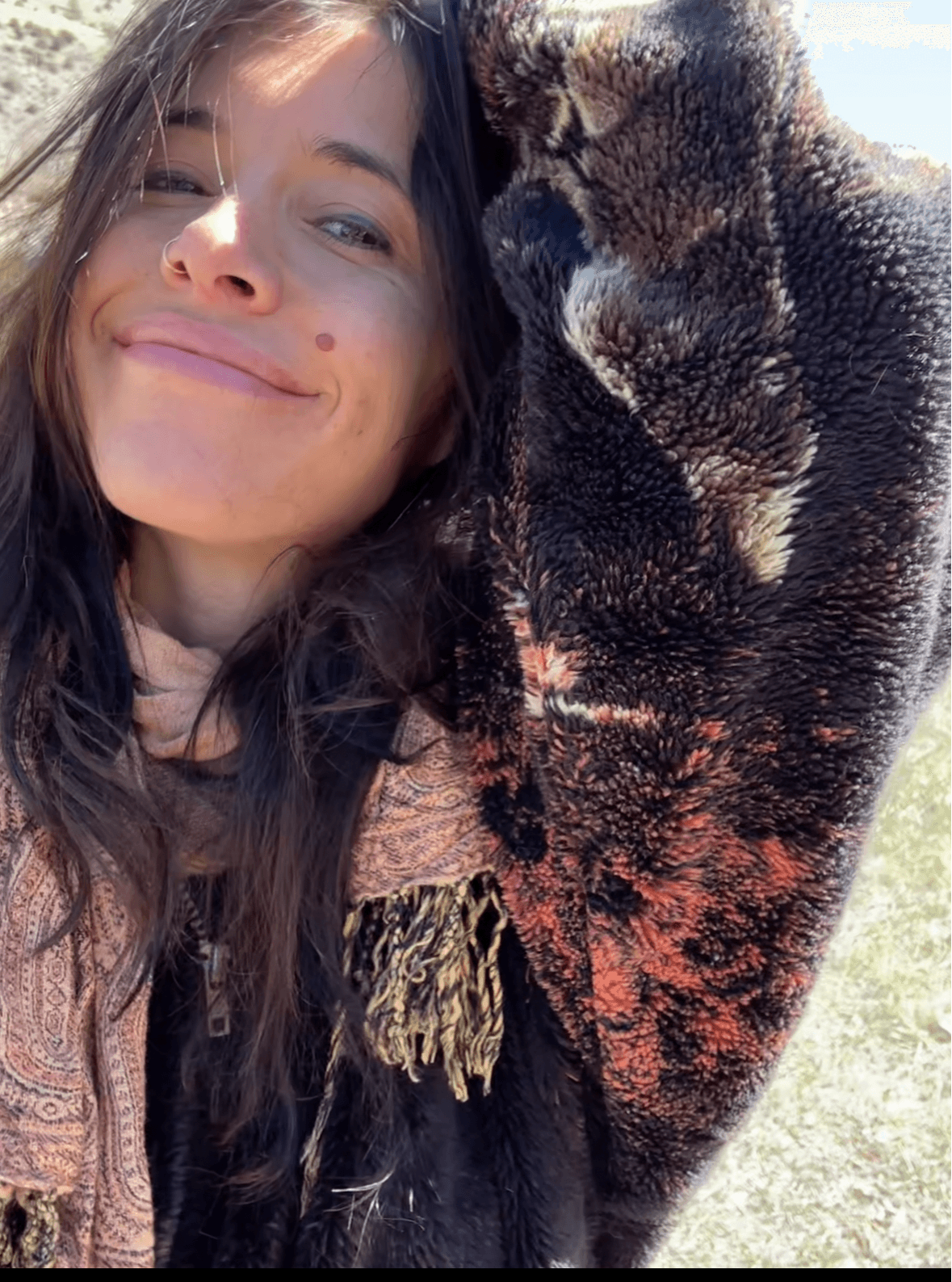 Young woman smiling outdoors with a large dog, both close together, sunny day, background of grass and sky.