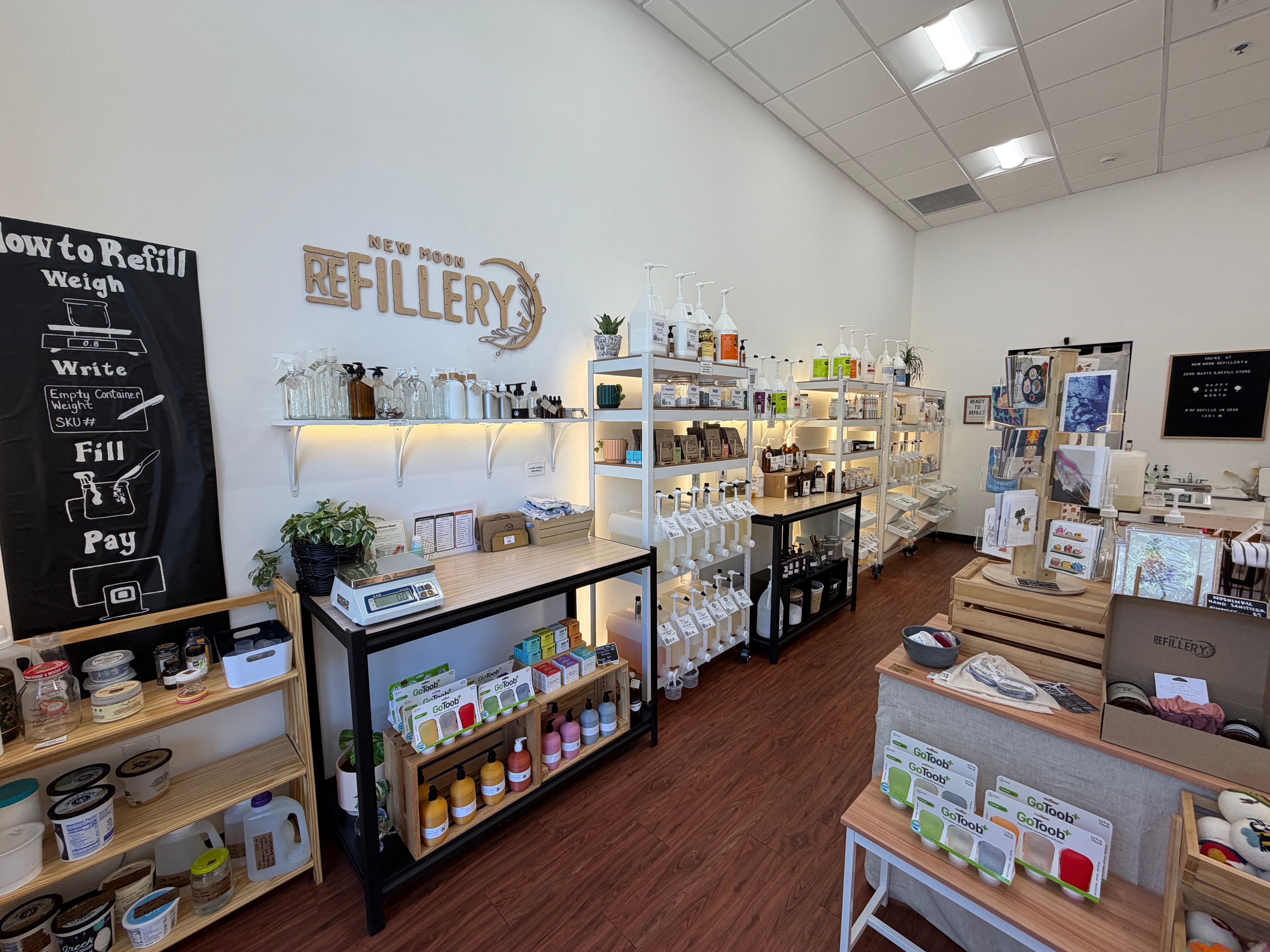 Interior of a refill store with shelves stocked with bottles, jars, and refill products, and a blackboard on the wall.