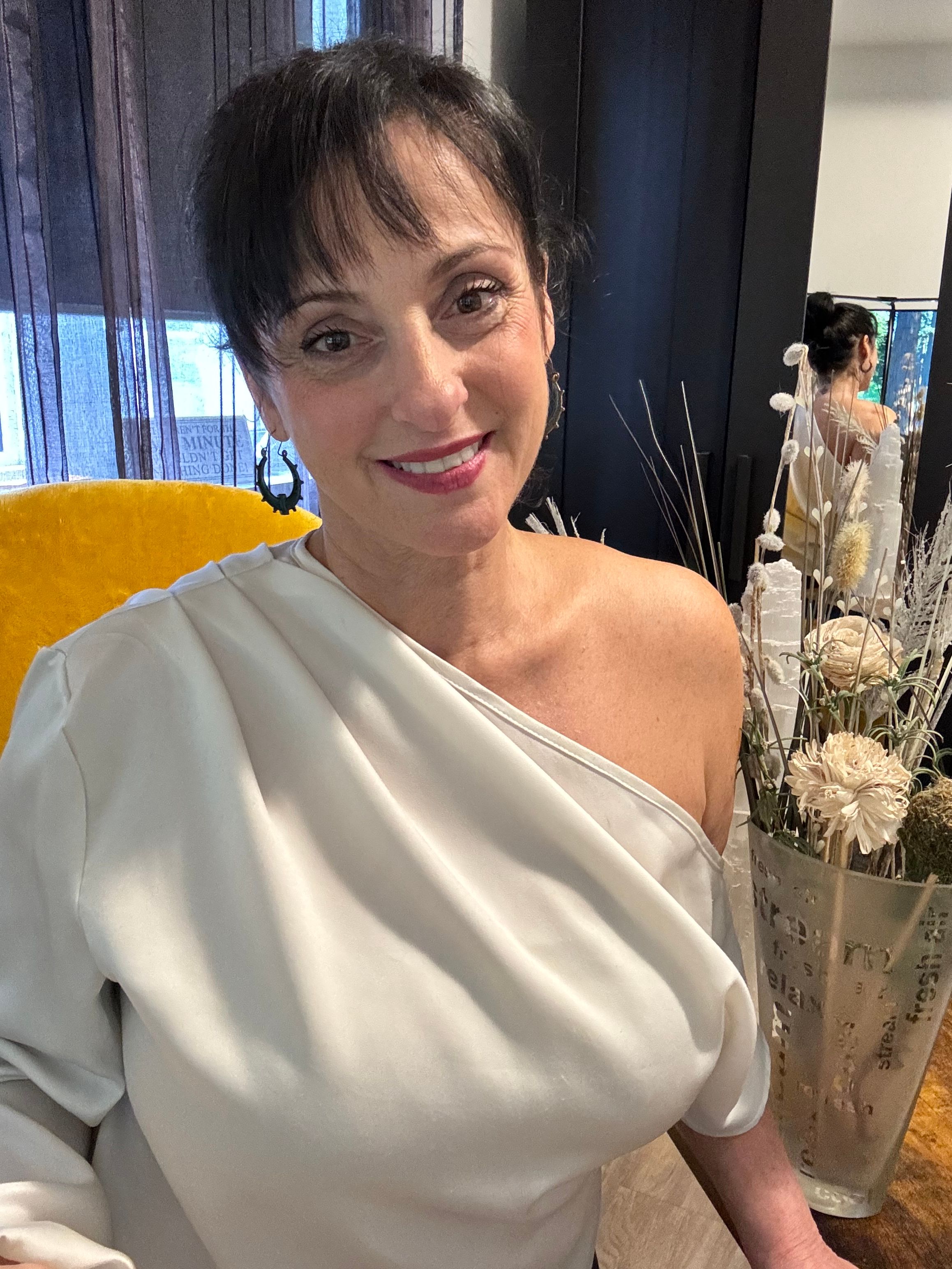 Woman in white dress smiling, with dark hair styled up, in a decorated indoor setting.