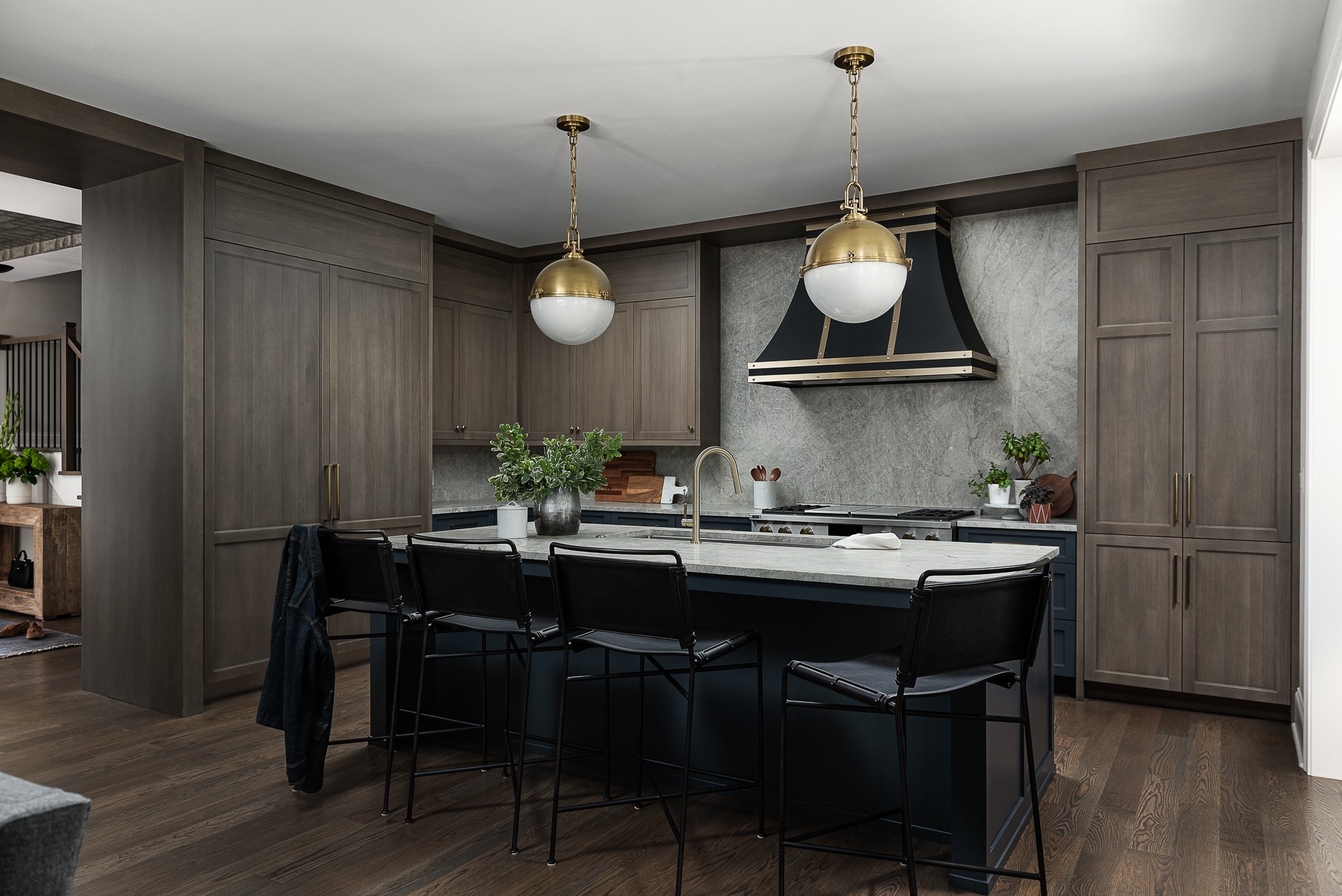 Modern kitchen with gray cabinets, black island, pendant lights, and a range hood, with a dining table and chairs.