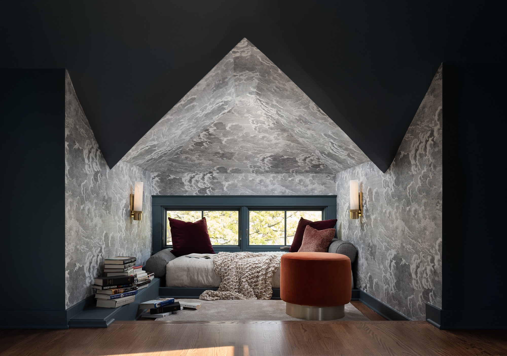 Bedroom with a window, bed, pillows, books, and a small orange chair under a sloped ceiling.