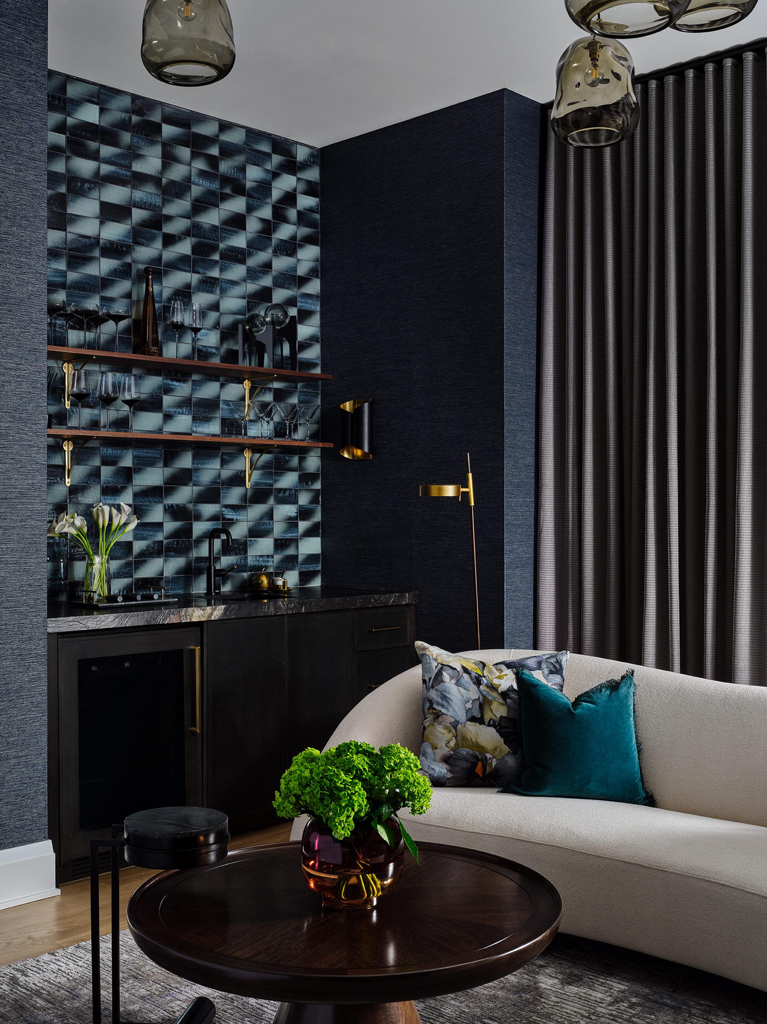 Living room corner with dark patterned wall, black shelves, white sofa with pillows, round table with green plant, and curtains.