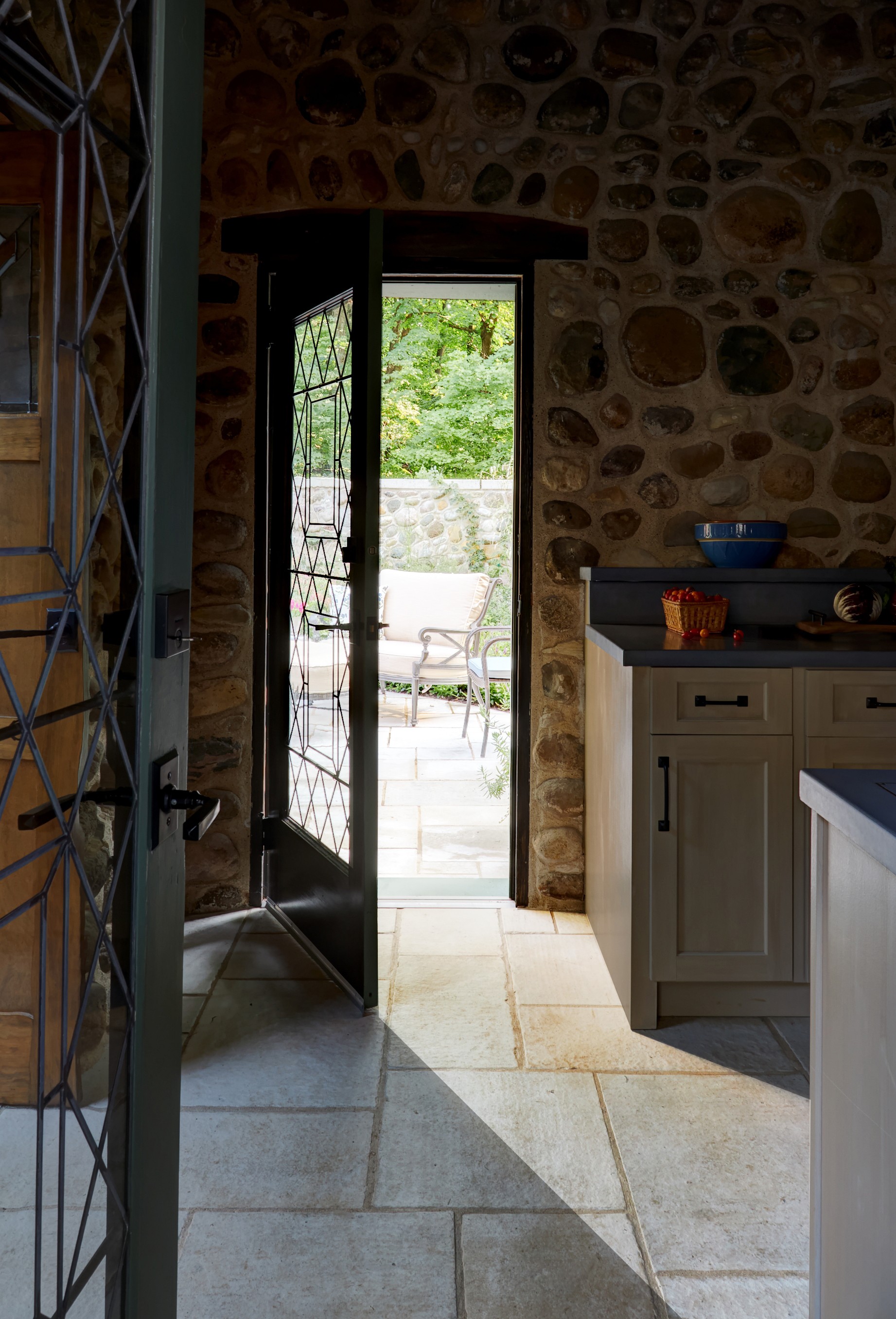 Open door leading outside to a patio with chairs, stone wall interior, and kitchen cabinet visible inside.