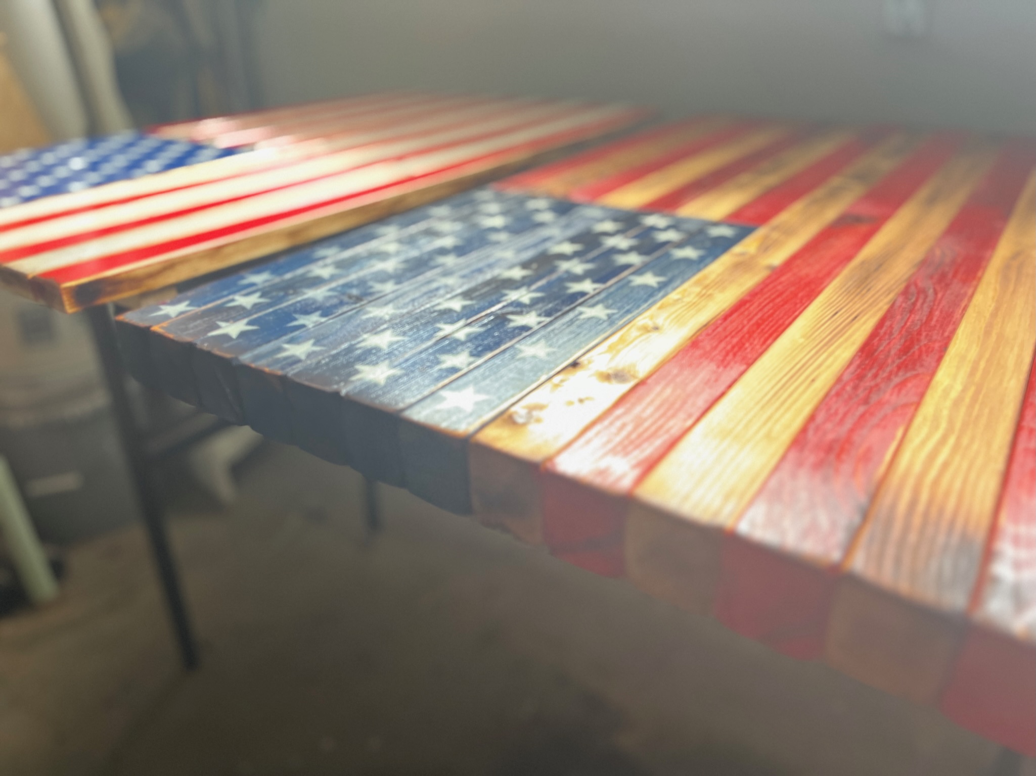 Wooden table with a painted American flag design, featuring red and white stripes and a blue field with white stars, in a room.