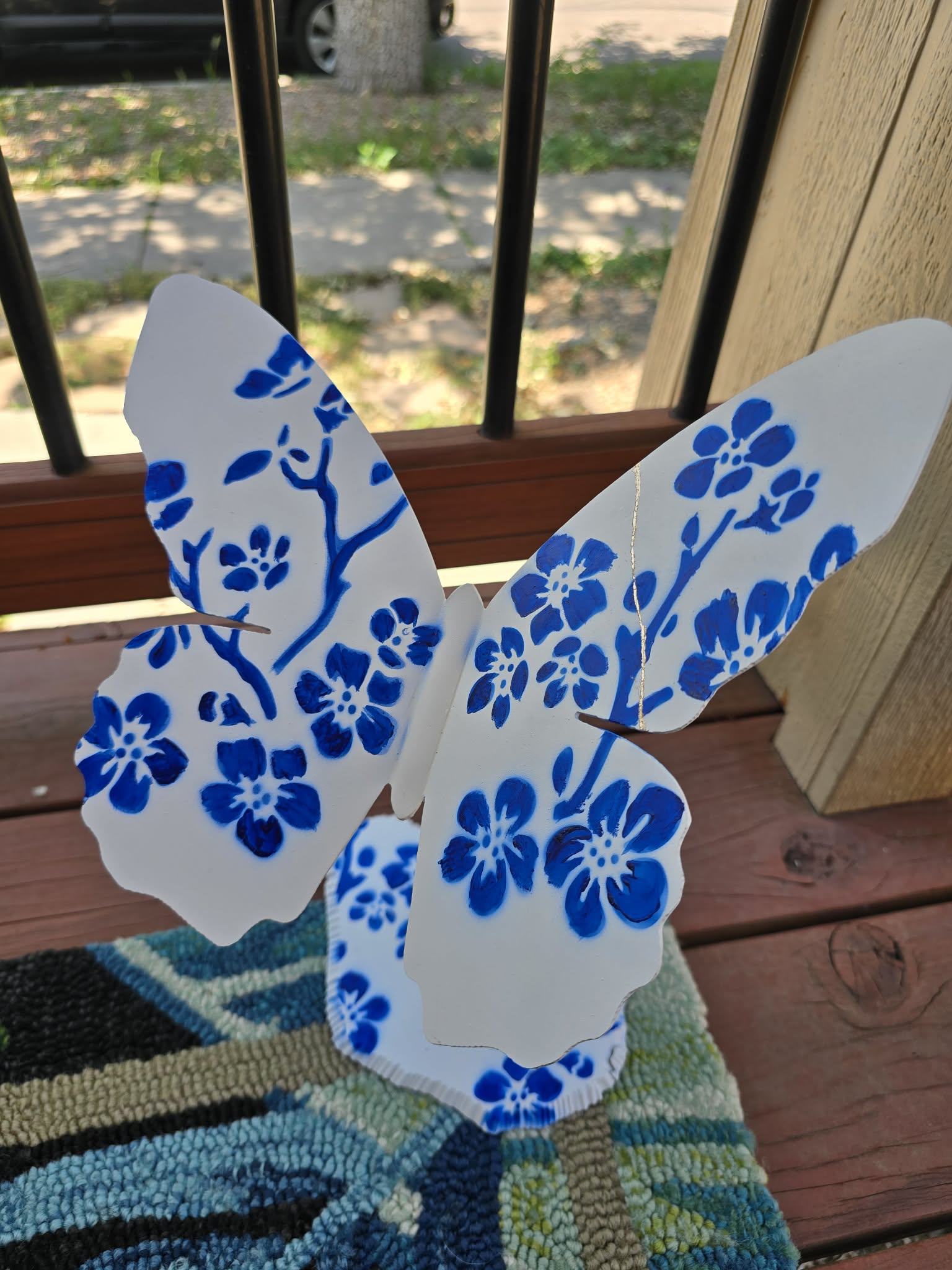 White butterfly cutout with blue floral pattern, placed on a wooden surface near a window with black bars.