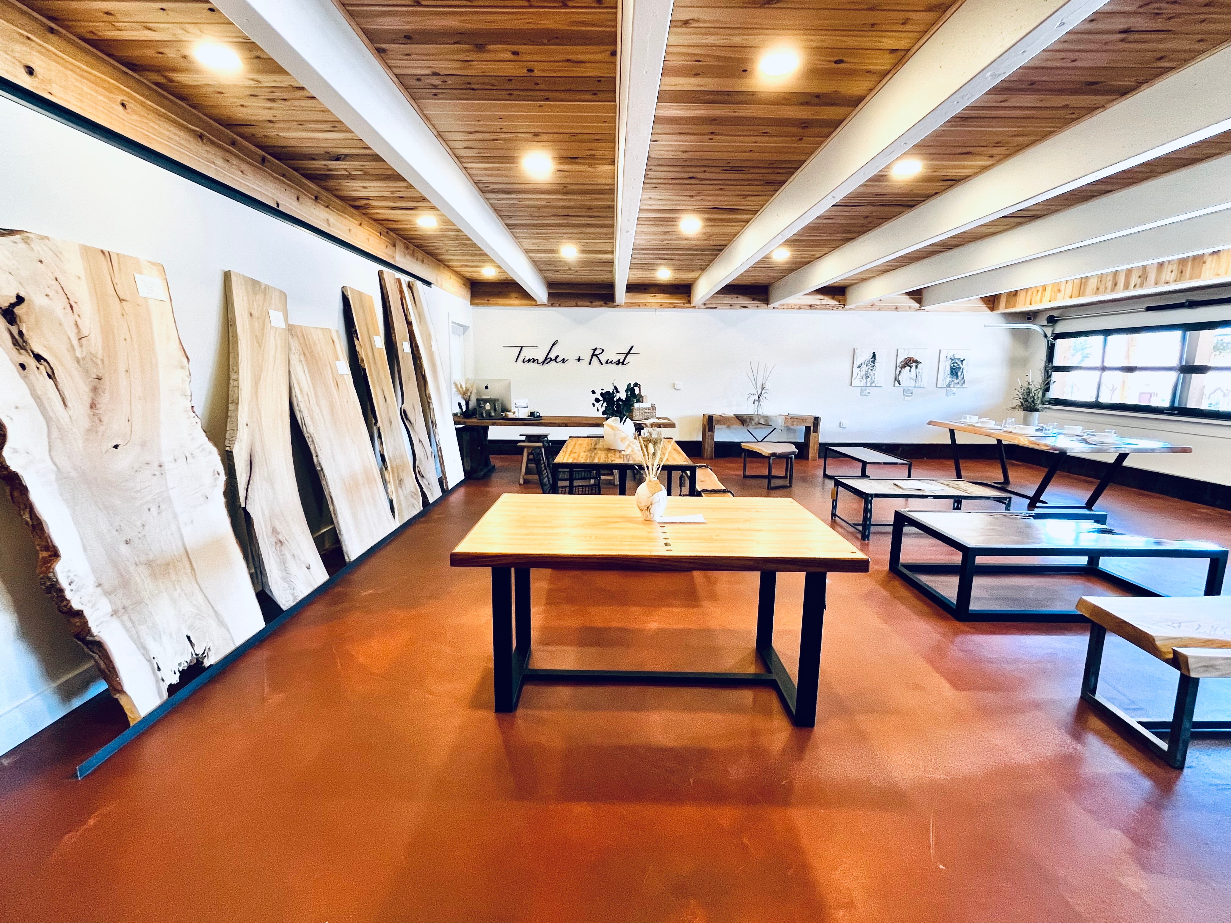 Art studio with large wood panels leaning against the wall, wooden tables, and benches, under a wooden ceiling with lighting.