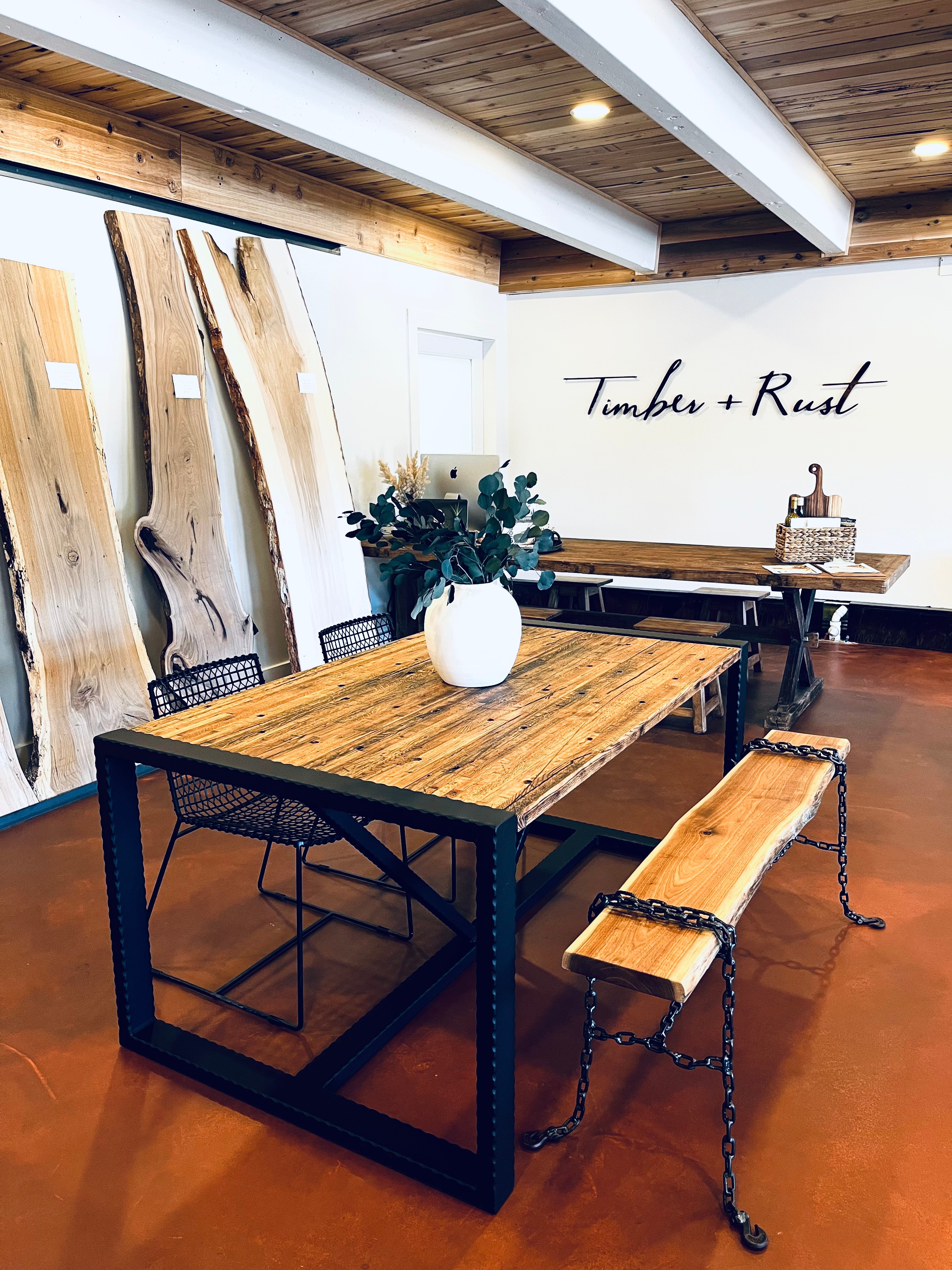 Wooden table with a white vase and flowers, surrounded by chairs, in a room with wood and white walls.