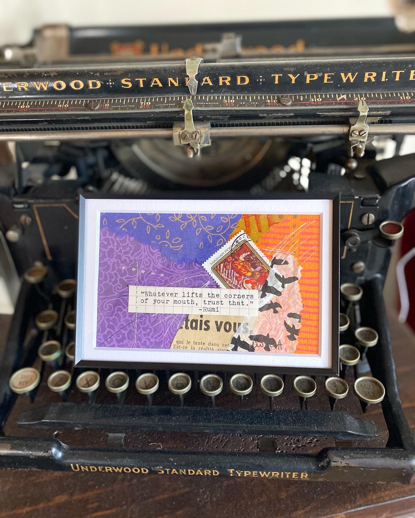 Typewriter with a colorful collage of paper and a small card inside the carriage, viewed from above.