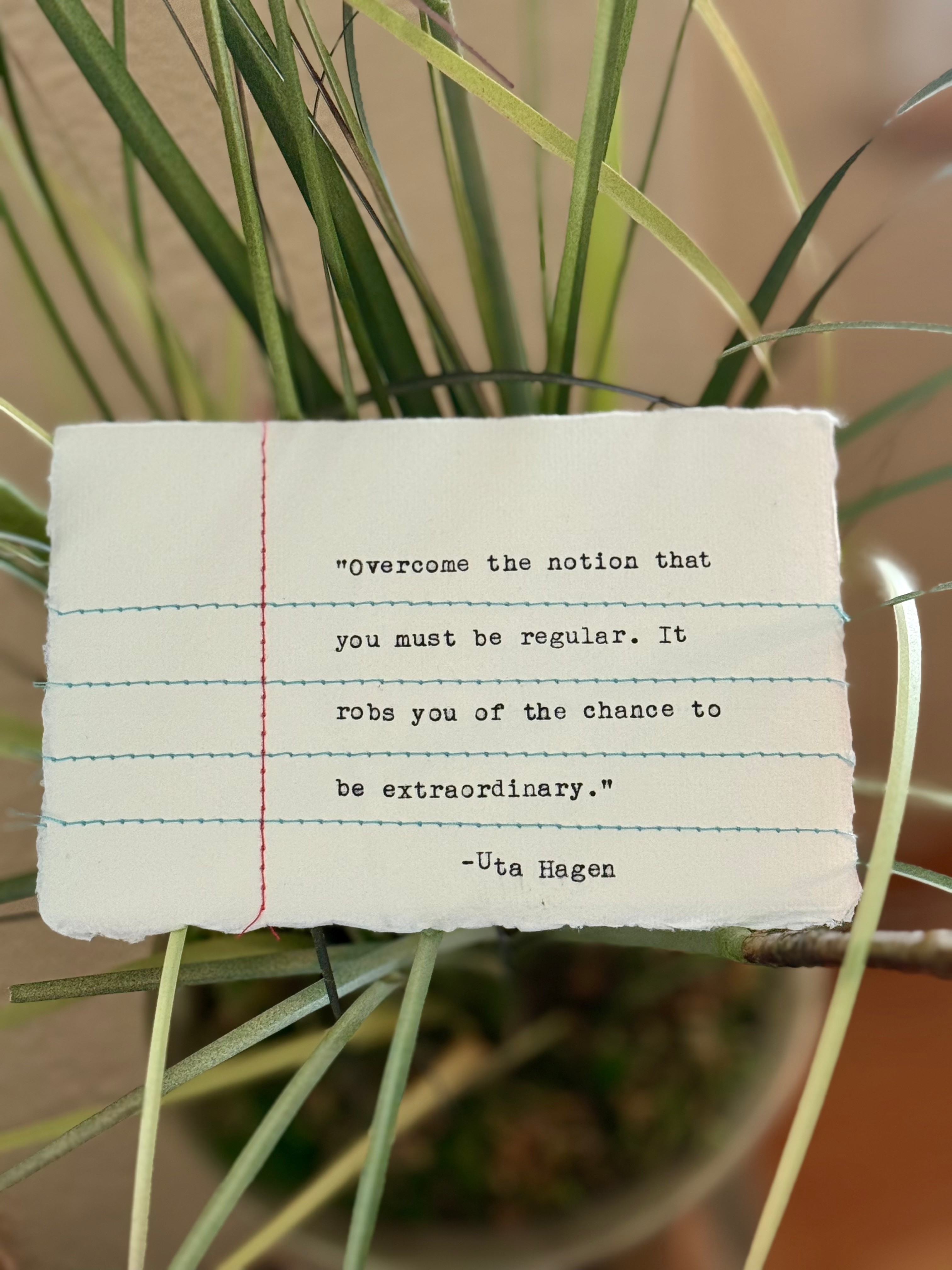 A torn piece of paper with a quote, held among green grass, with a blurred background.