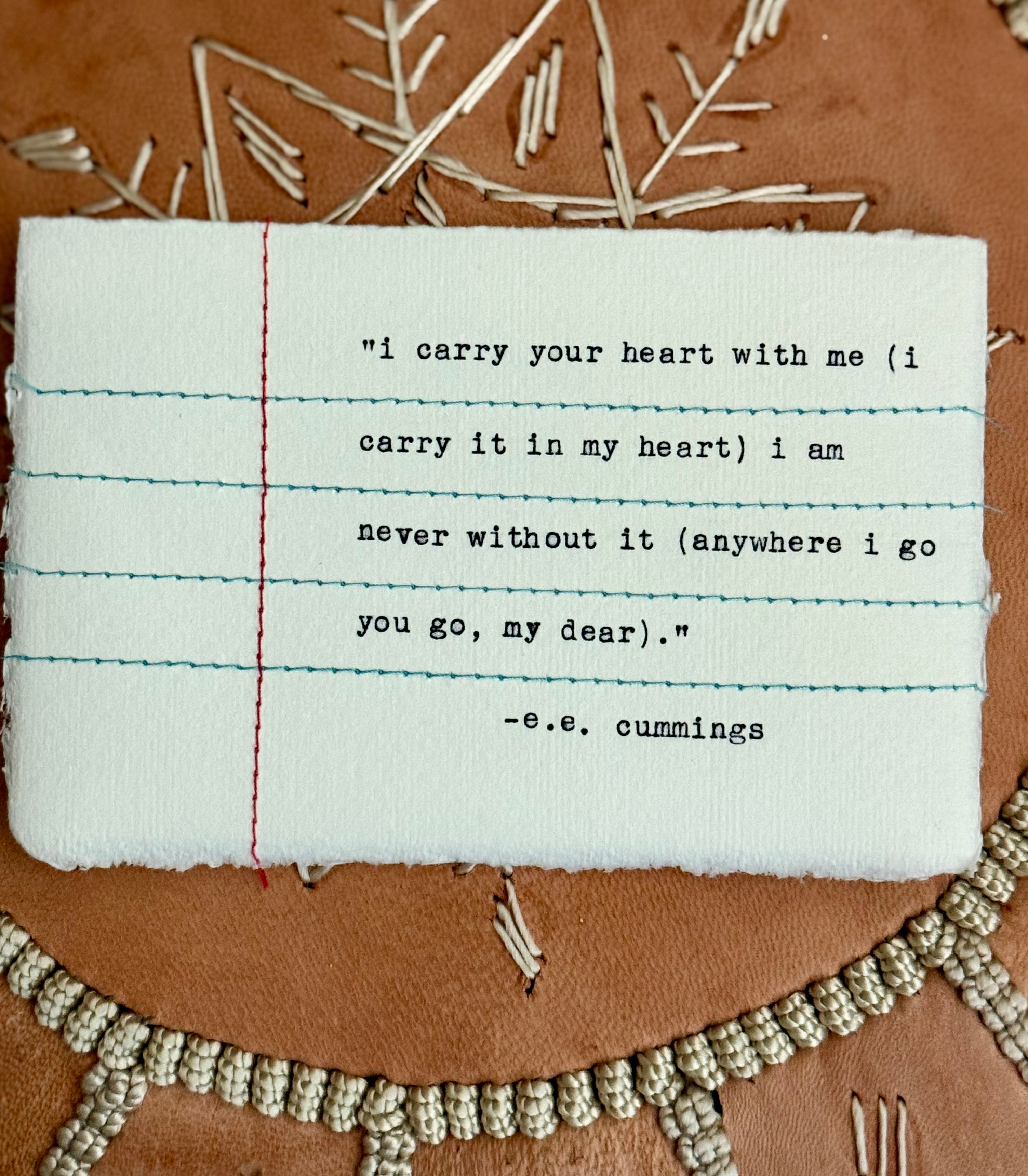A piece of fabric with a quote about carrying a heart, placed on a brown surface with decorative beads and dried plant material.