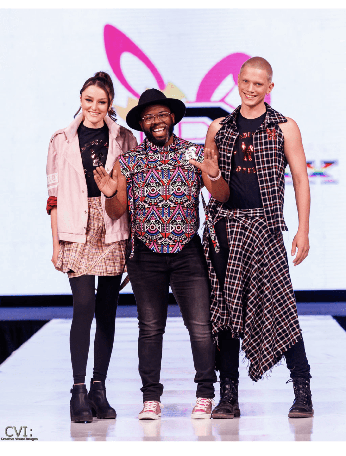 Three people standing together on a runway, smiling, with a colorful background behind them.