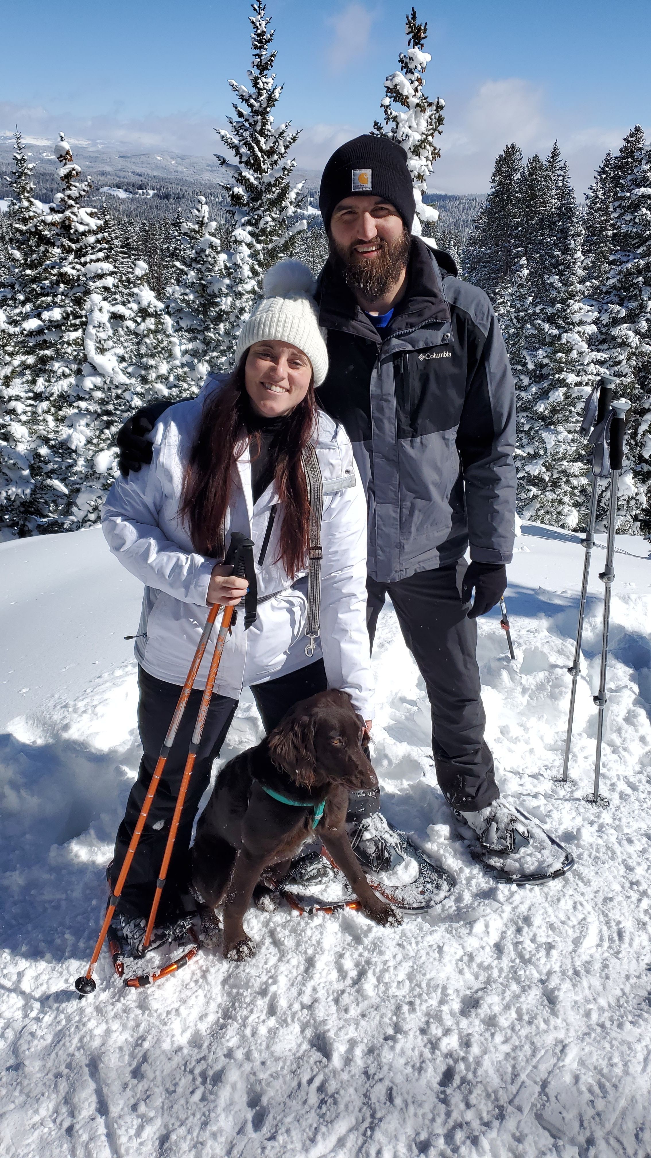 Group of four people outdoors in snowy landscape, with trees and sky in background, smiling and posing for photo.