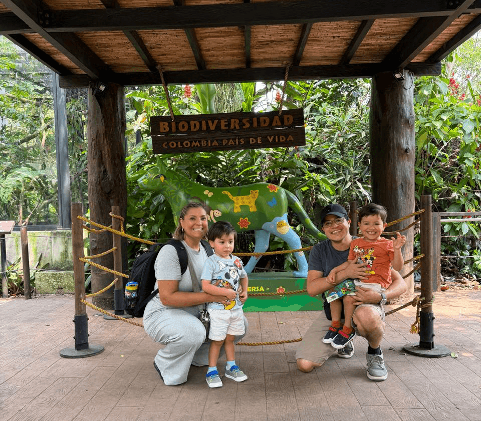 Family of four with two children posing in front of a colorful animal sculpture at a biodiversity exhibit, surrounded by greenery.