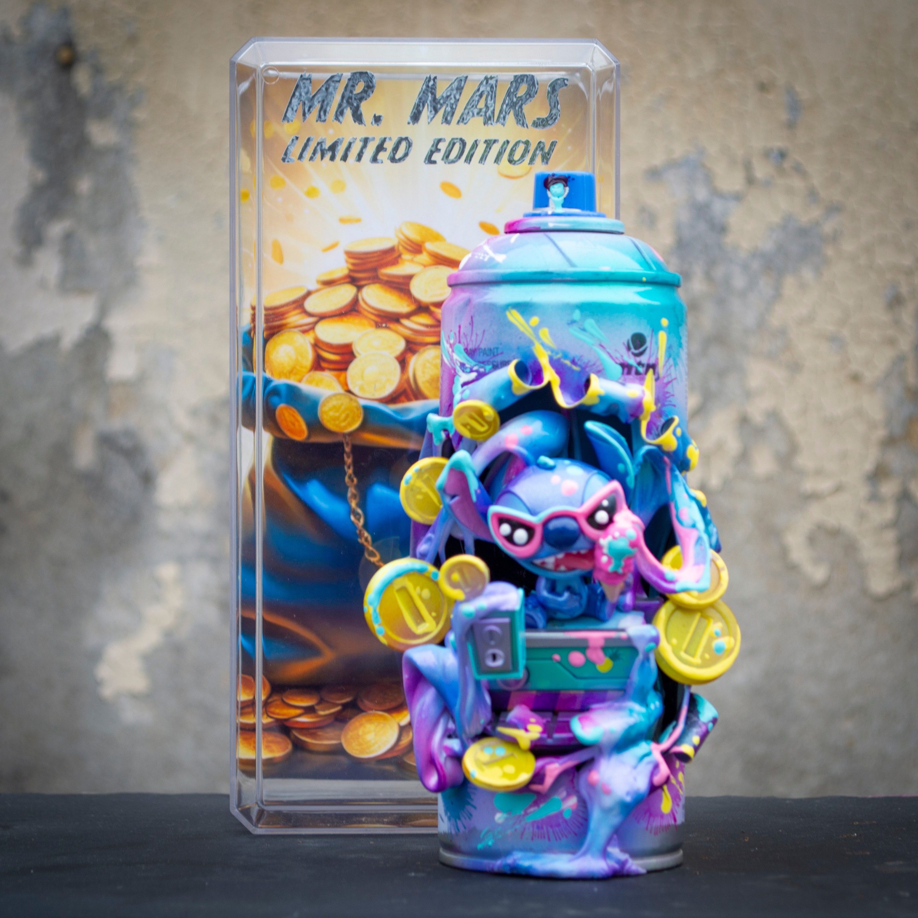 Colorful Mr. Mars limited edition collectible figure with coins, in front of a transparent box with coins and text, on a black surface.