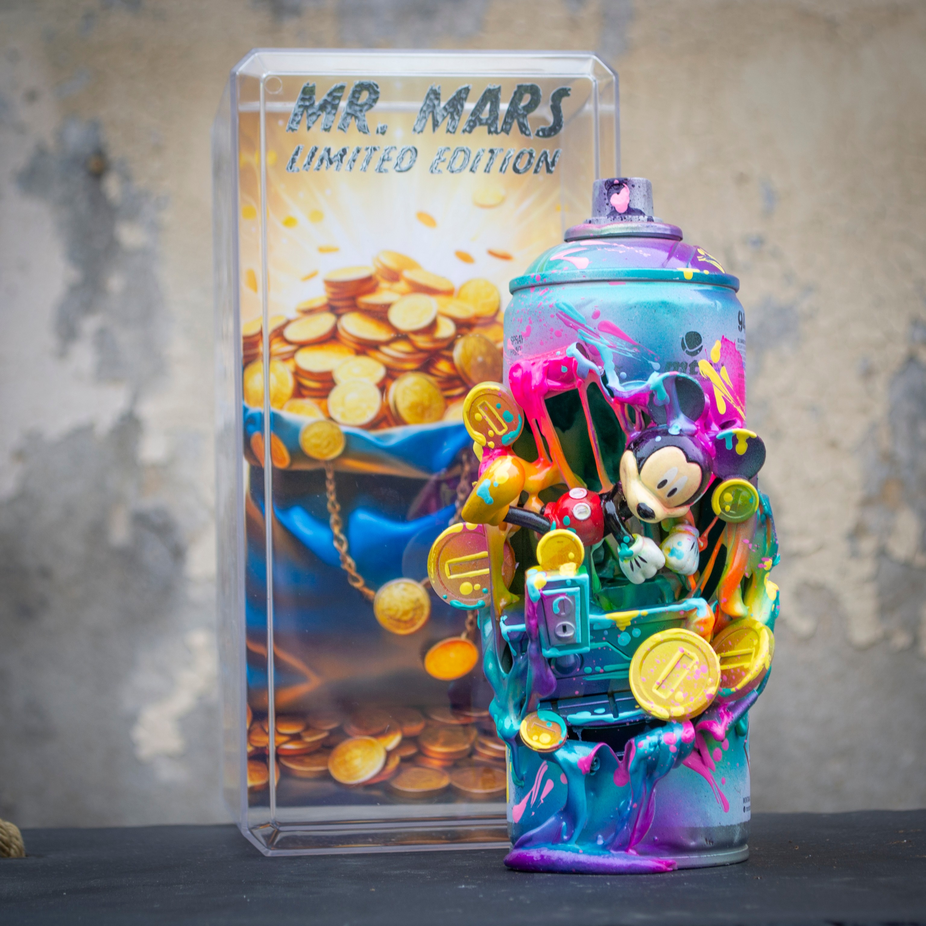 Colorful can with toys and slime, transparent display case with coins and text, on a black surface against a gray wall.