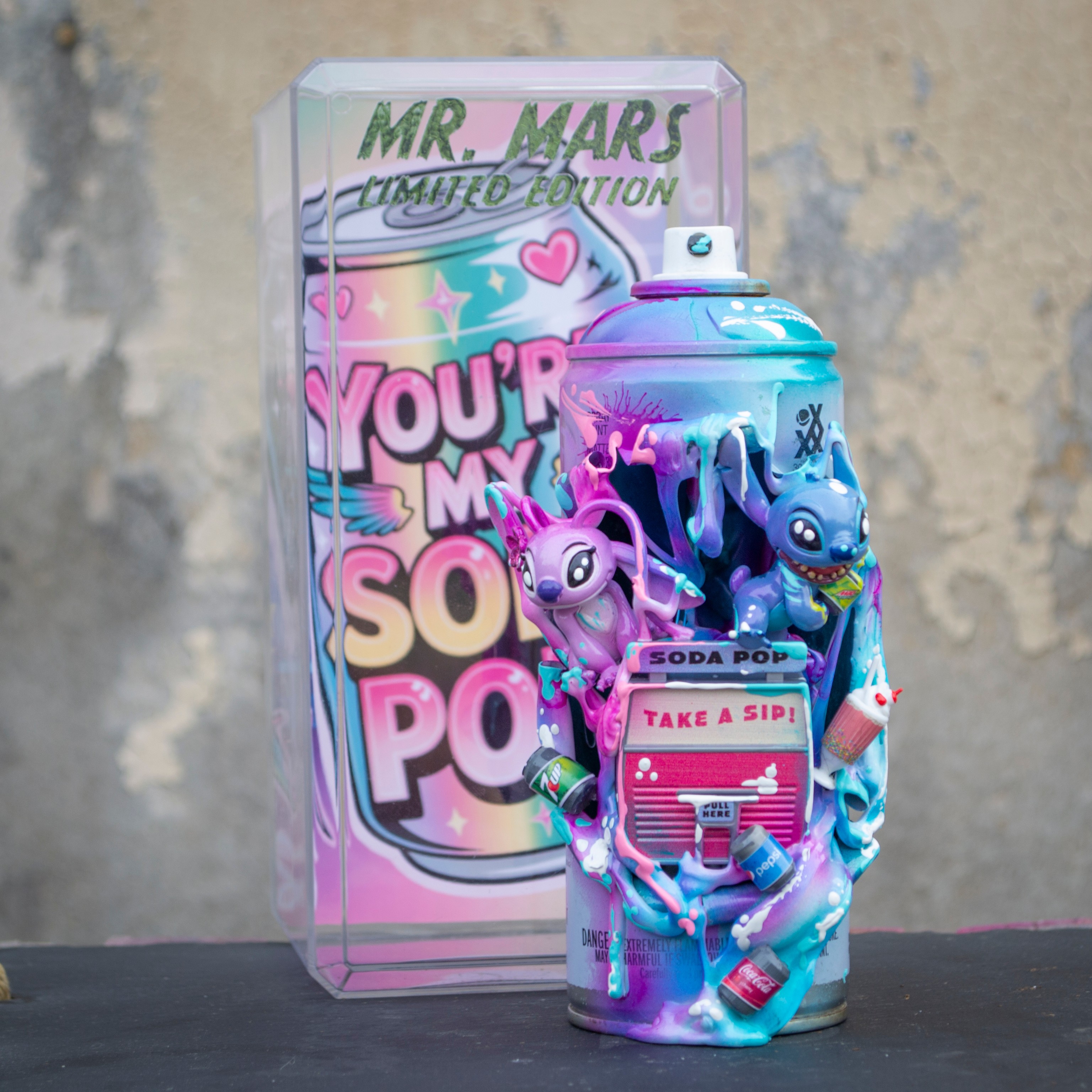 Colorful Mr. Mars toy with characters and a soda pop theme, in front of a vibrant packaging box, on a black surface.