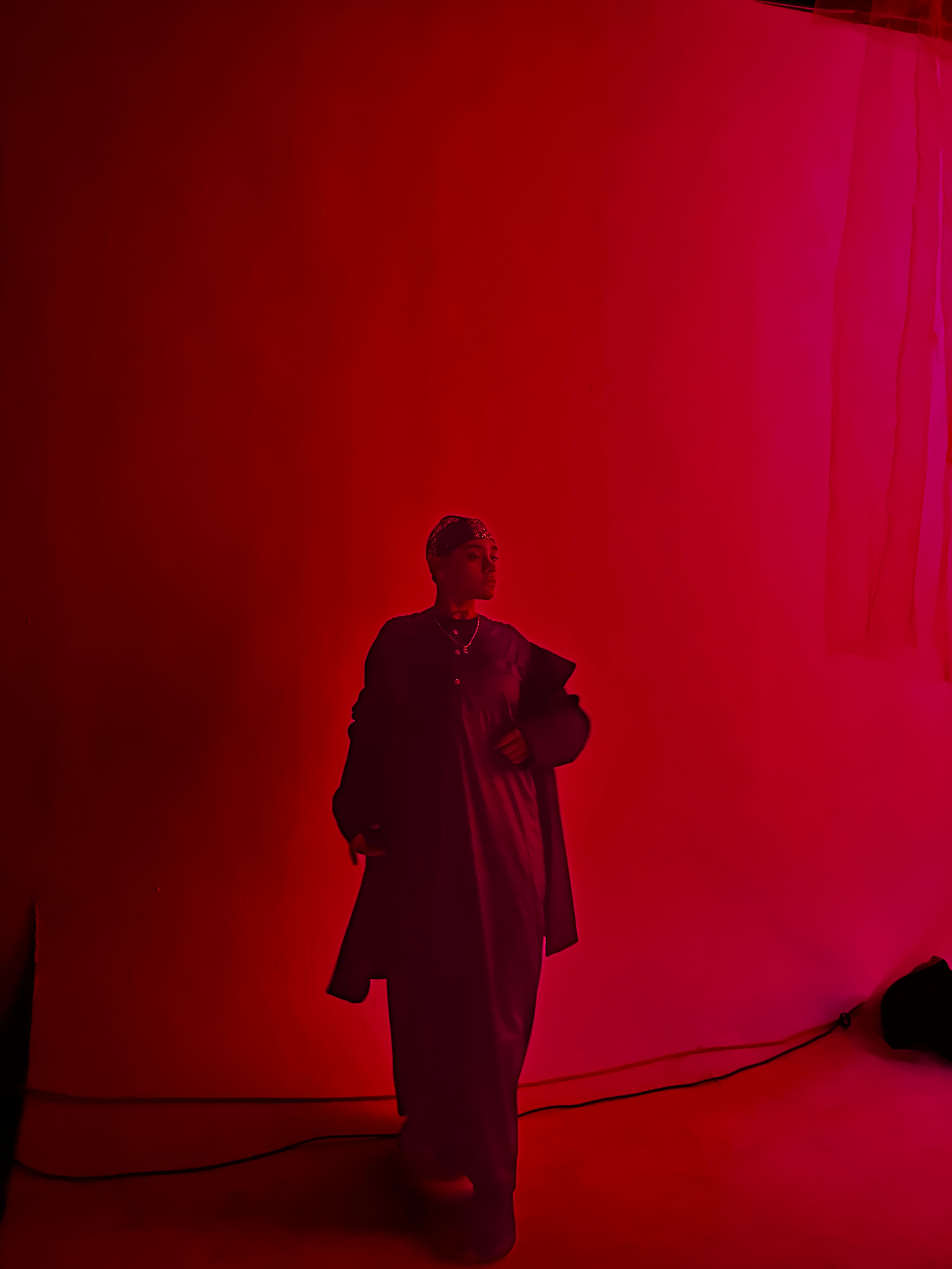Person standing on stage with a microphone, against a red background, holding a paper or book, with a cable nearby.