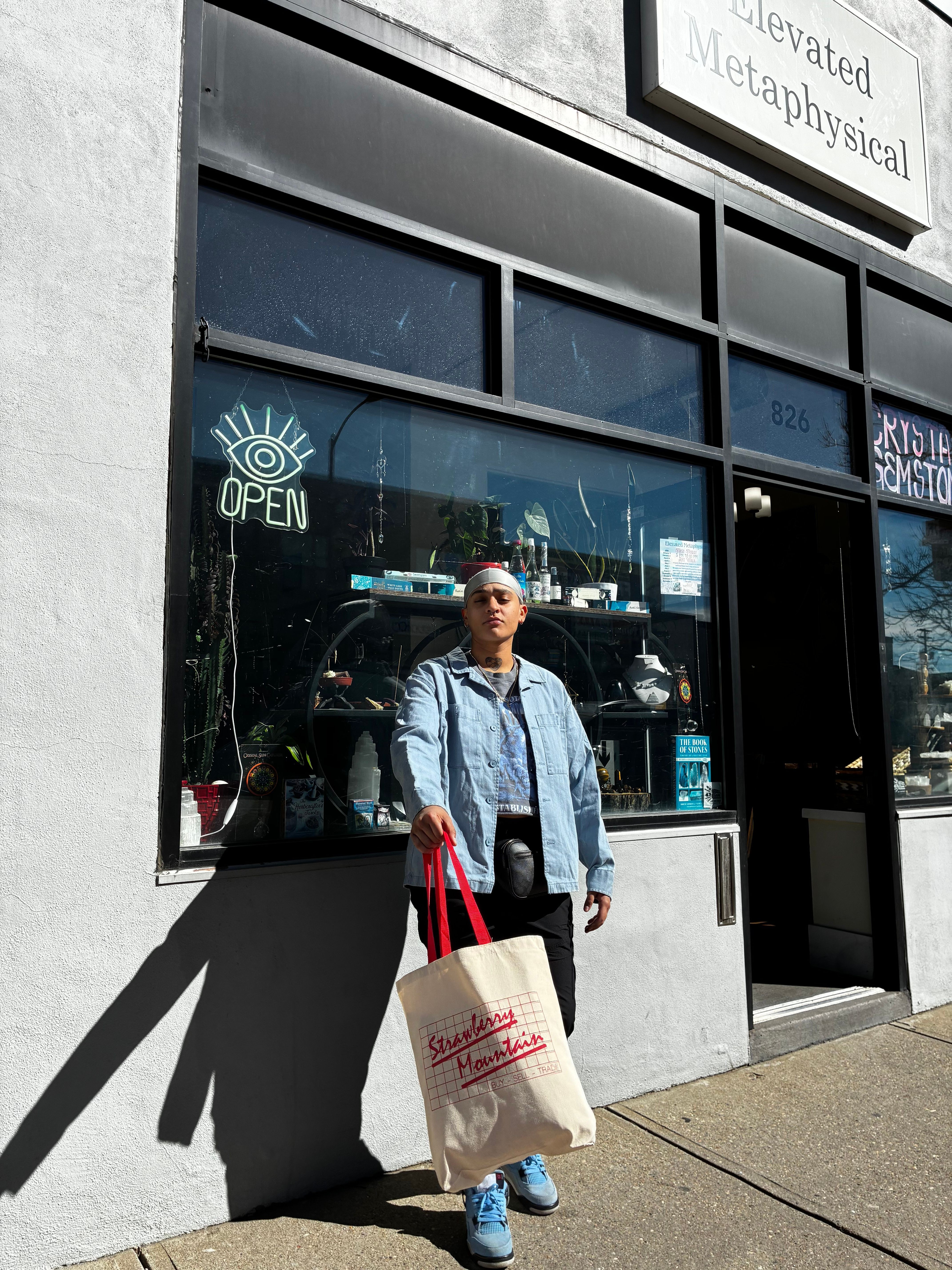 Person standing outside a building with large glass windows, holding a shopping bag, sunlight casting a shadow.