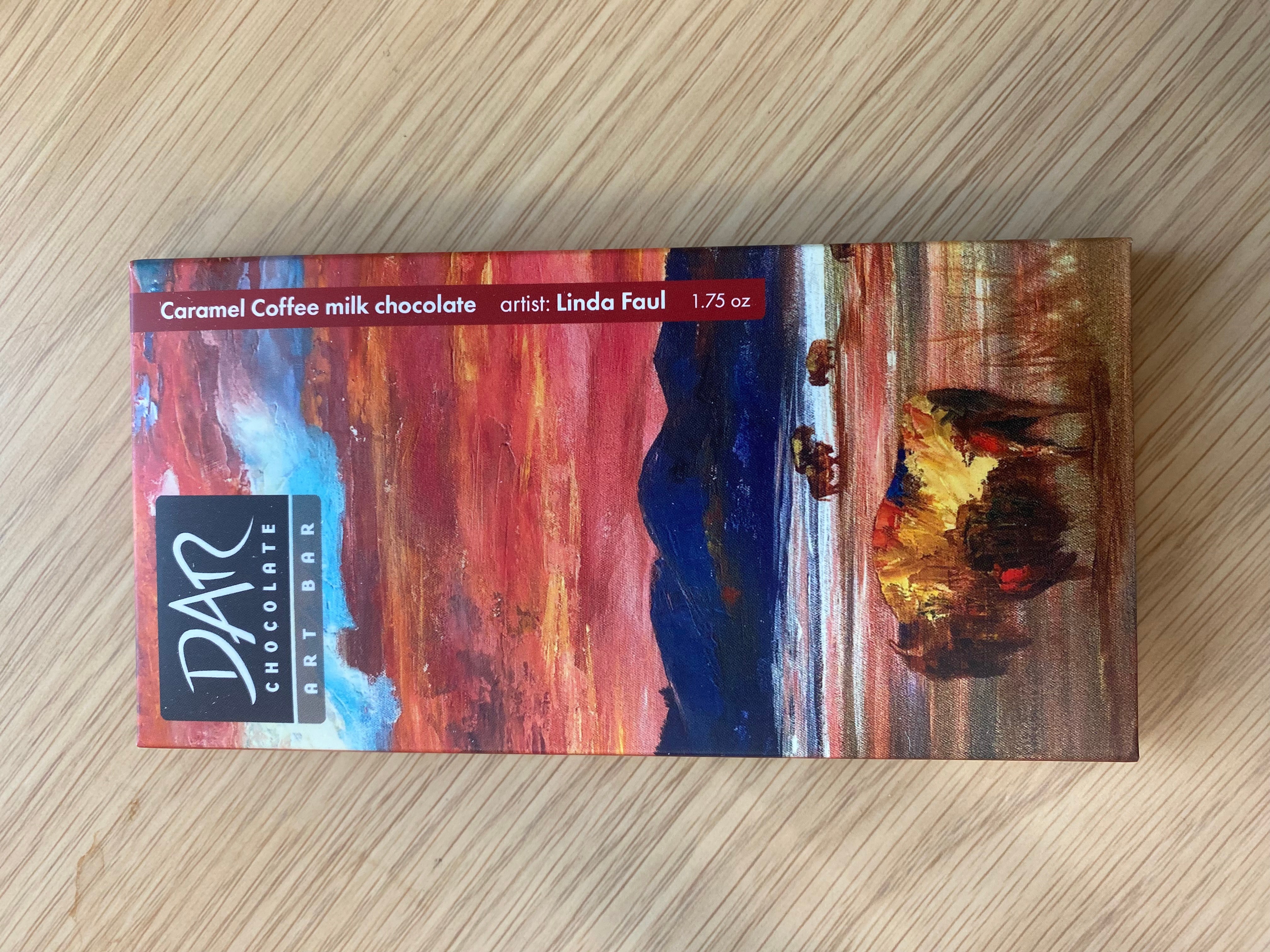 A rectangular box of caramel coffee milk chocolate with a colorful landscape painting on the packaging, including a sunset sky and mountains.