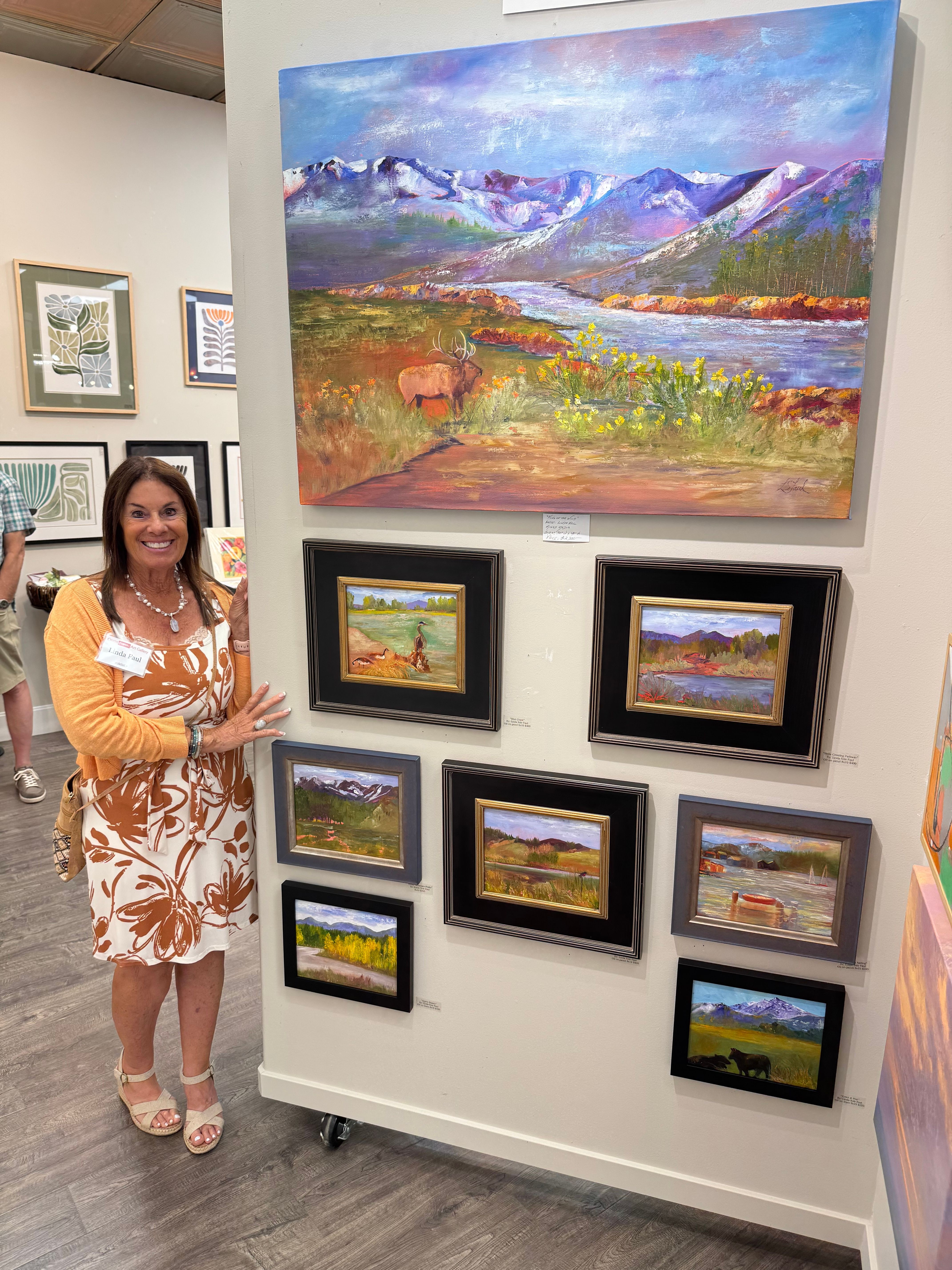 Woman in orange and white dress standing in an art gallery with framed paintings on white walls.