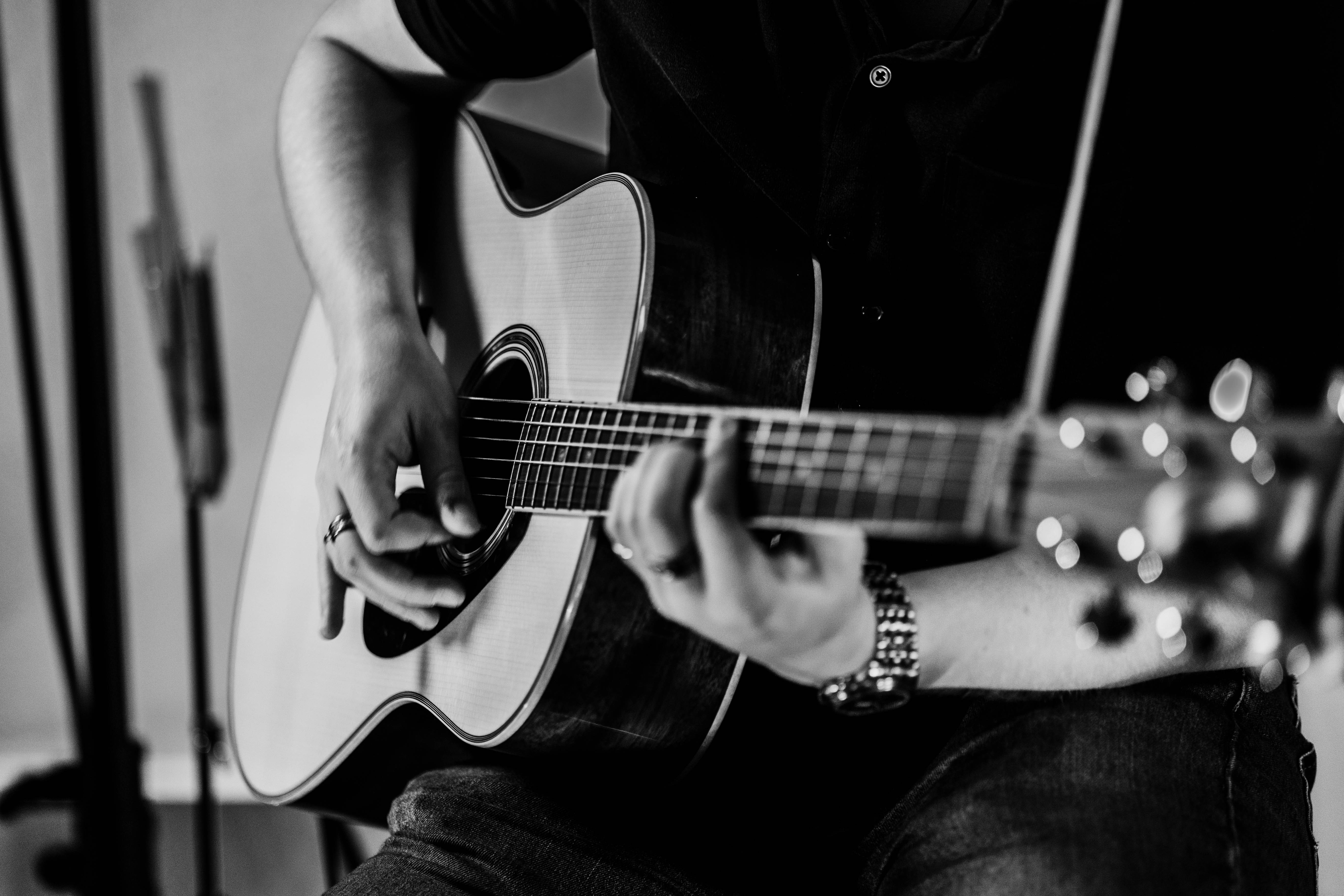 Person playing an acoustic guitar, focusing on hands and guitar, in black and white.