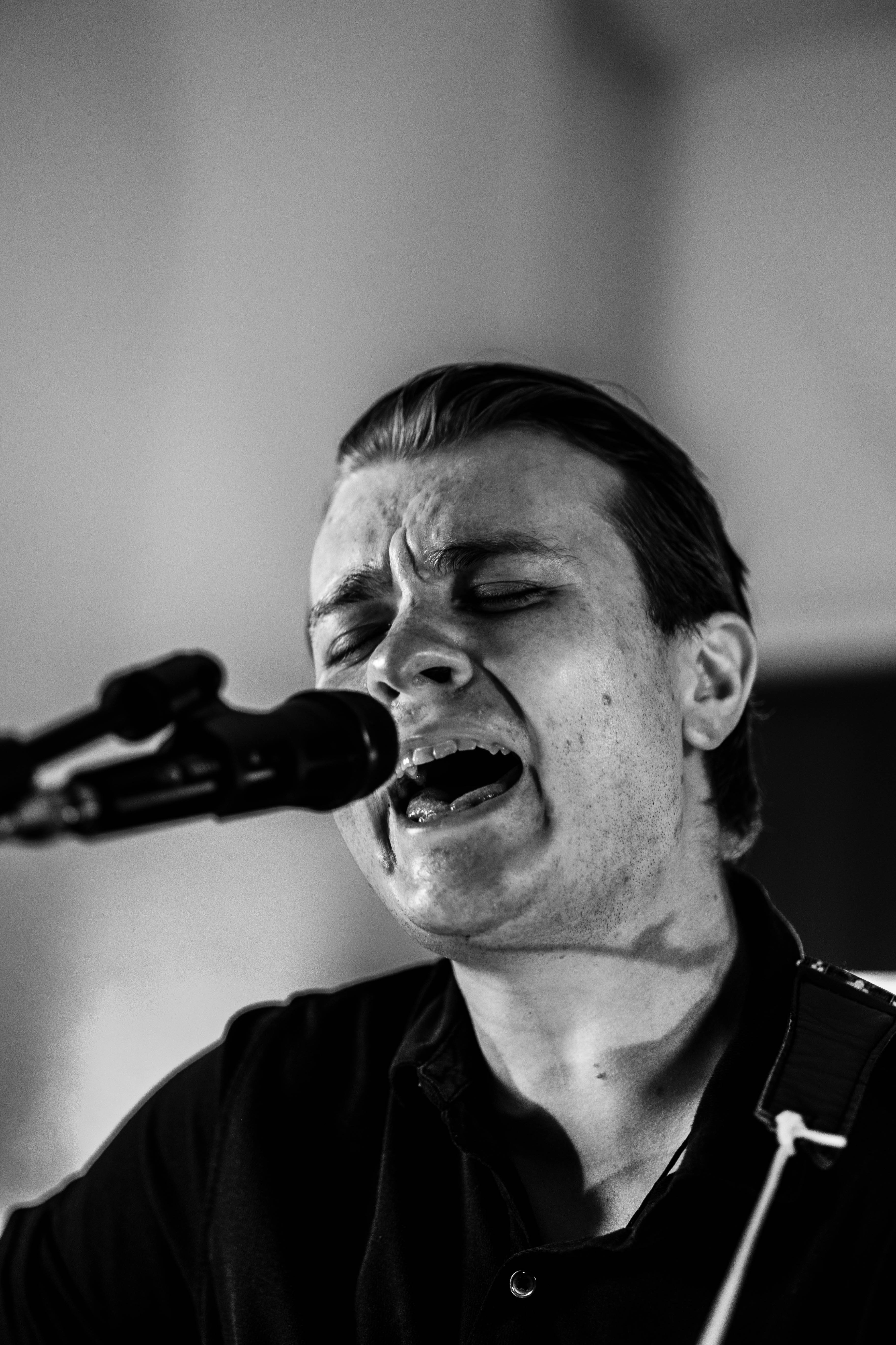 Person singing passionately into a microphone with eyes closed and facial expression showing emotion.