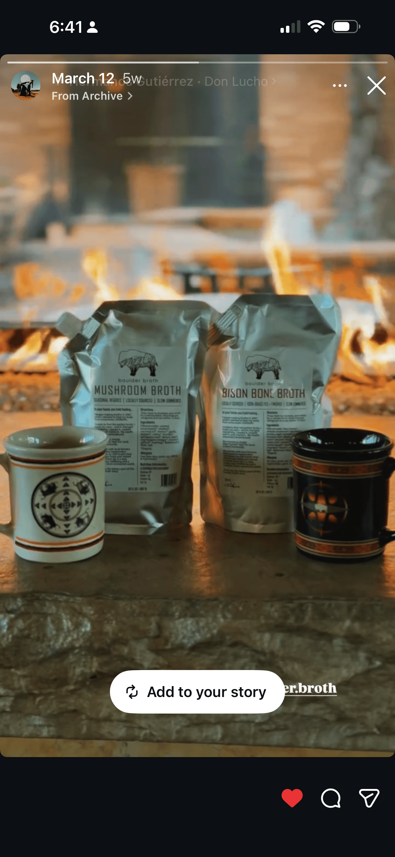 Two bags of coffee and two coffee cups on a table with a fire in the background.