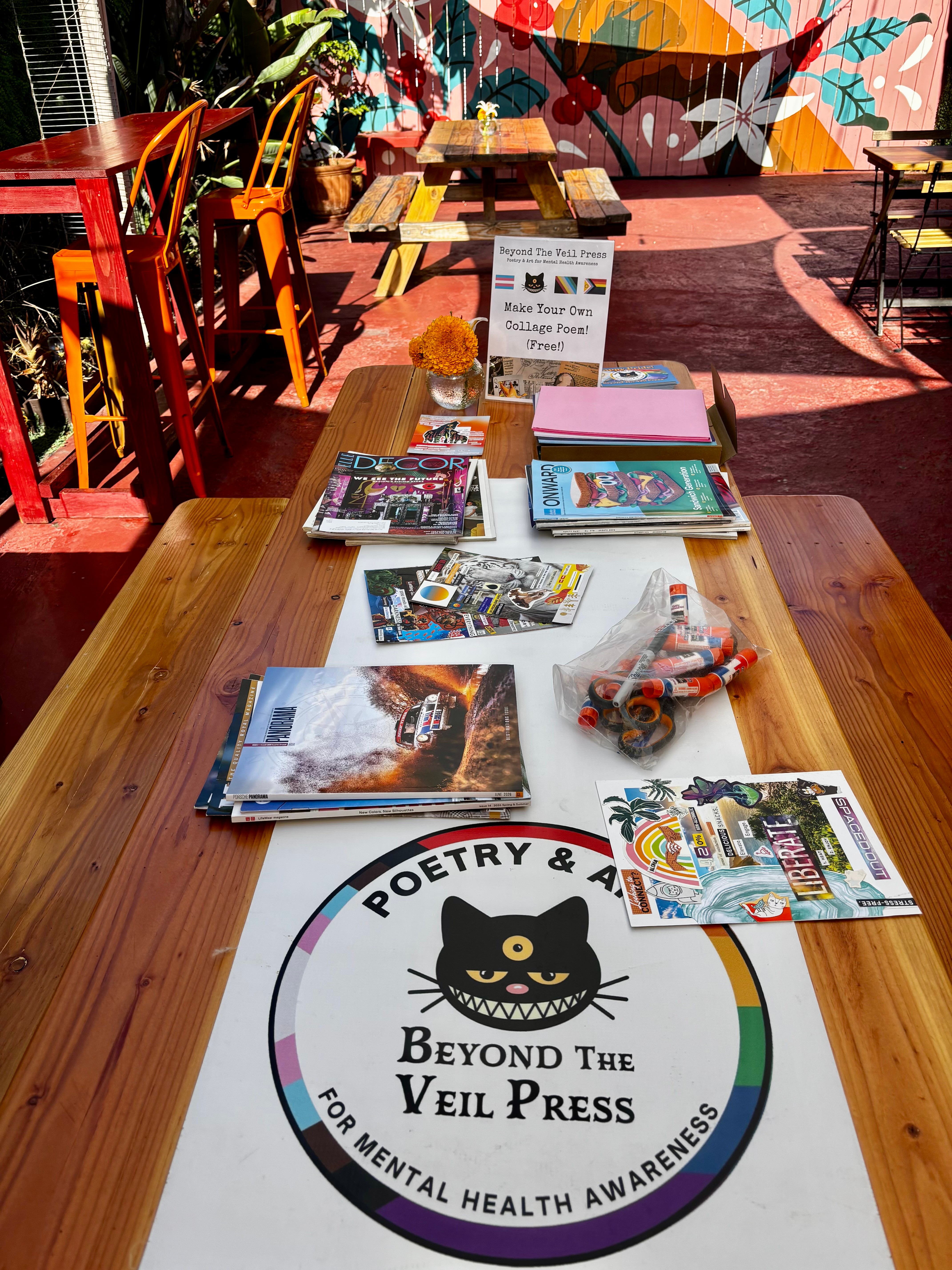 Long table with books and a circular sign promoting mental health awareness, colorful mural in background, outdoor setting.
