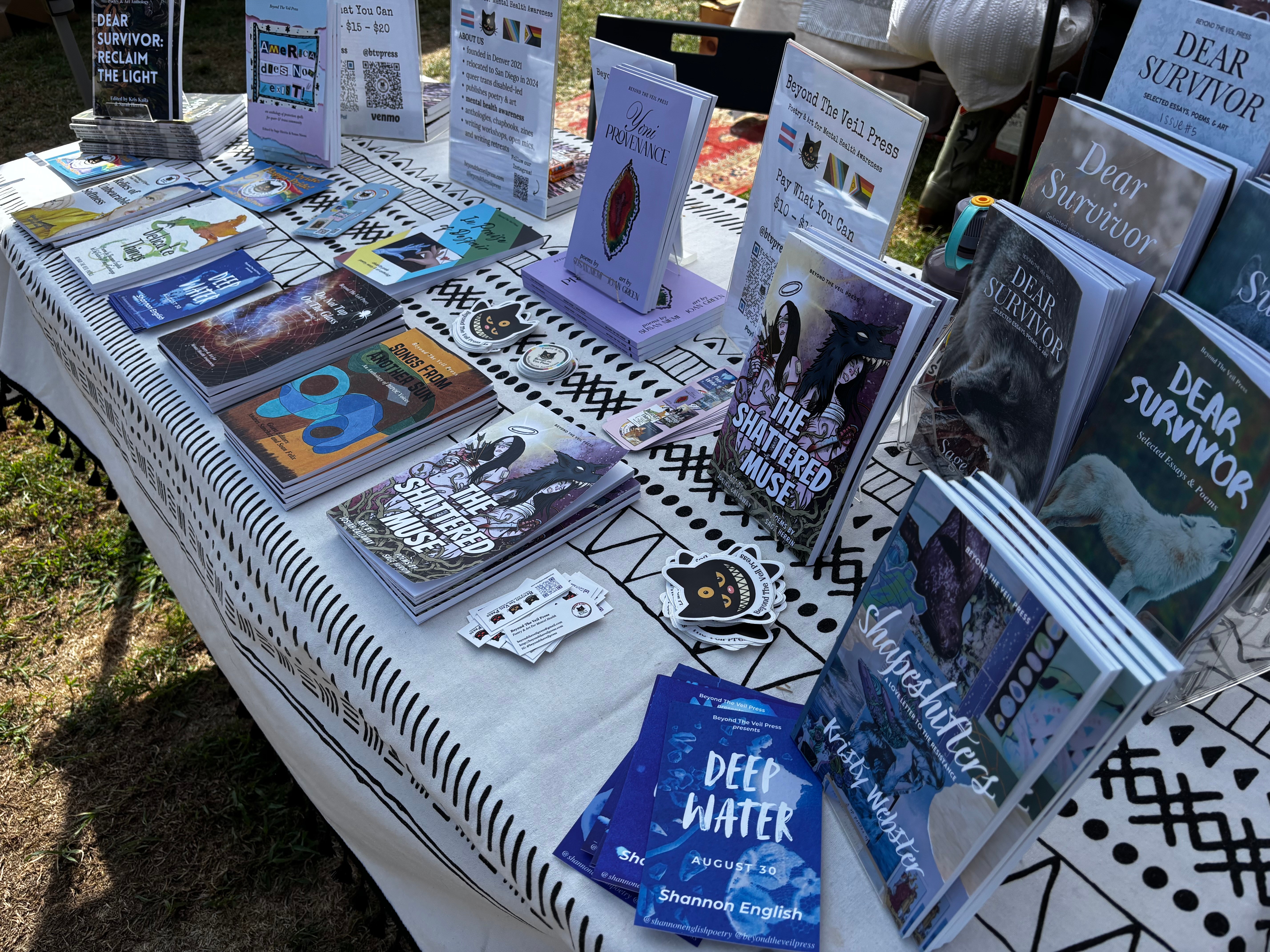 Table displays various books and pamphlets about survival and water, arranged on a patterned tablecloth outdoors.