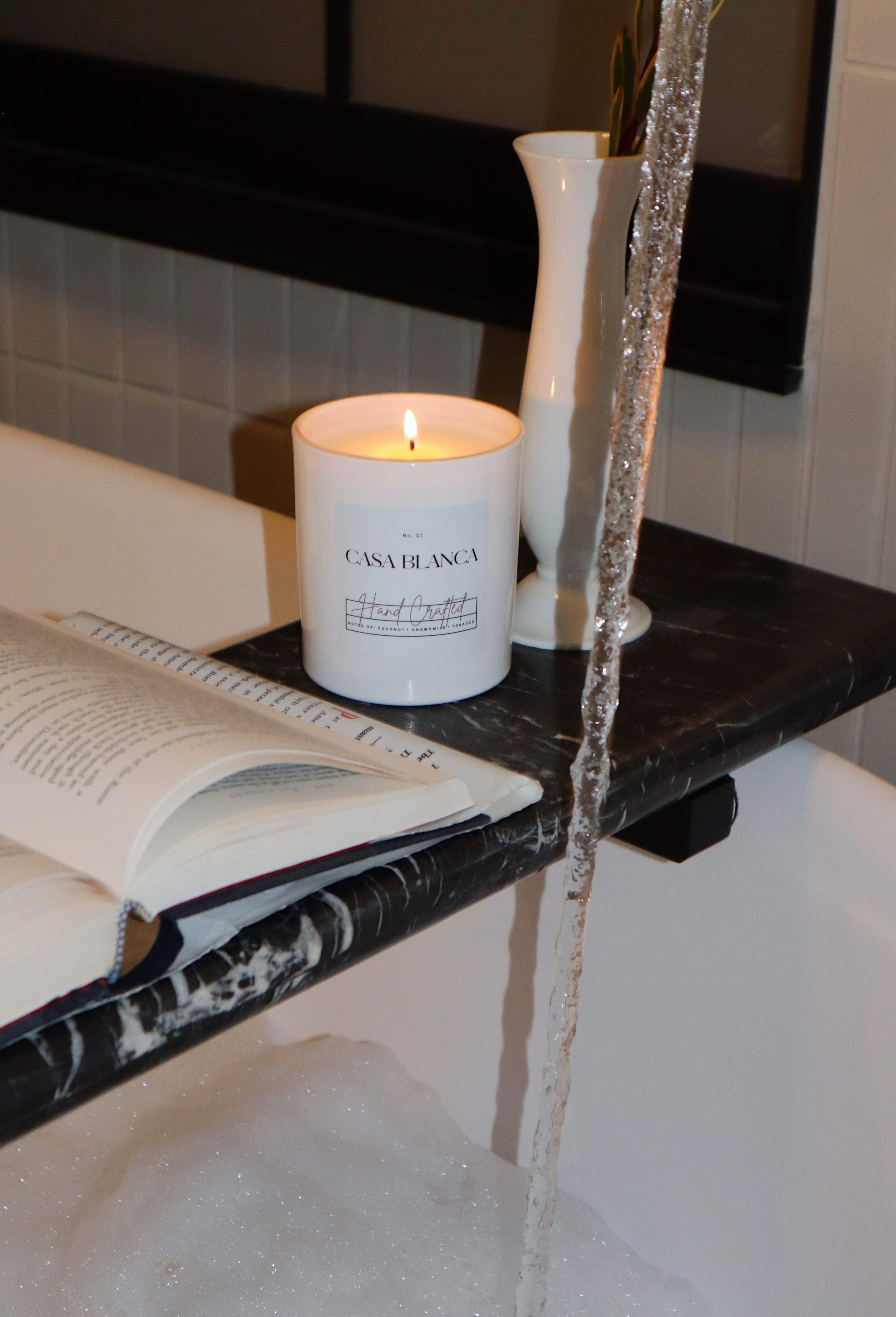 Lit candle, open book, and vases on a black marble shelf with water flowing down the side.