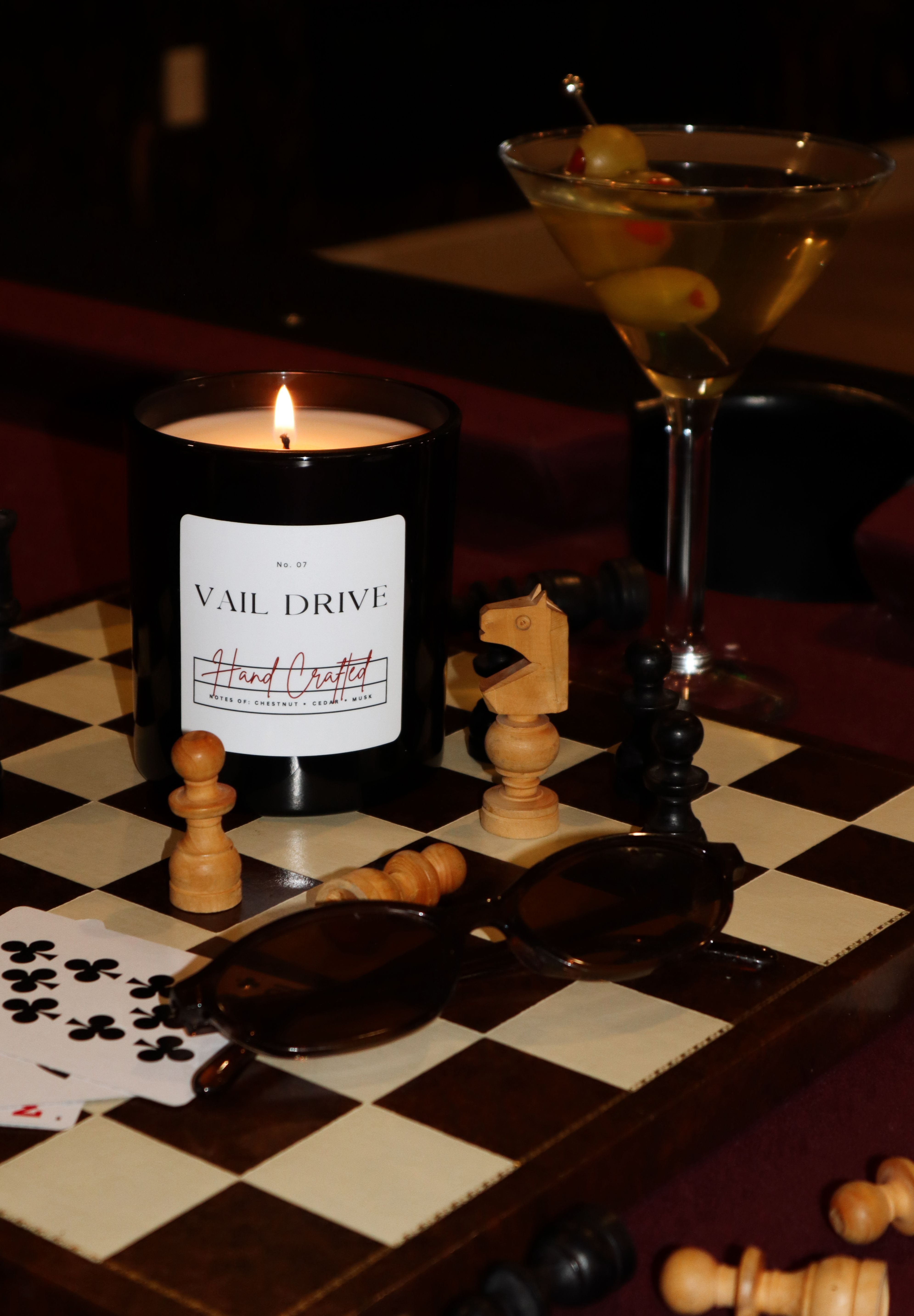 A candle shaped like a wine bottle, a pair of sunglasses, and chess pieces on a chessboard.