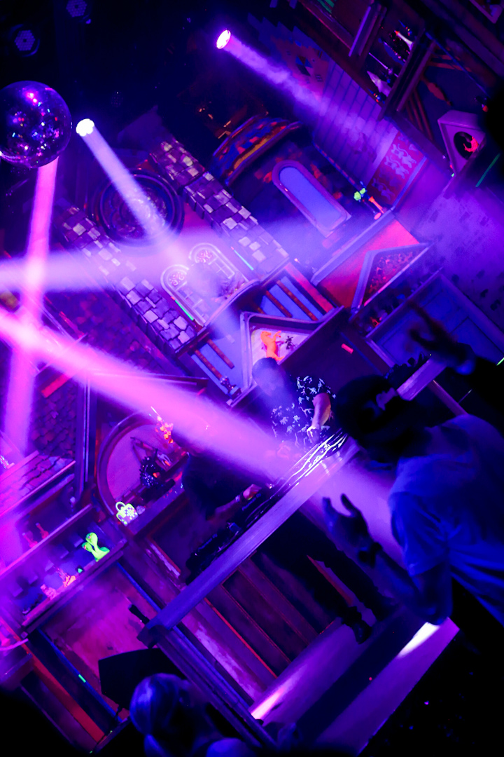 Nightclub scene with colorful lights, laser beams, and people dancing, illuminated by purple and blue lighting.