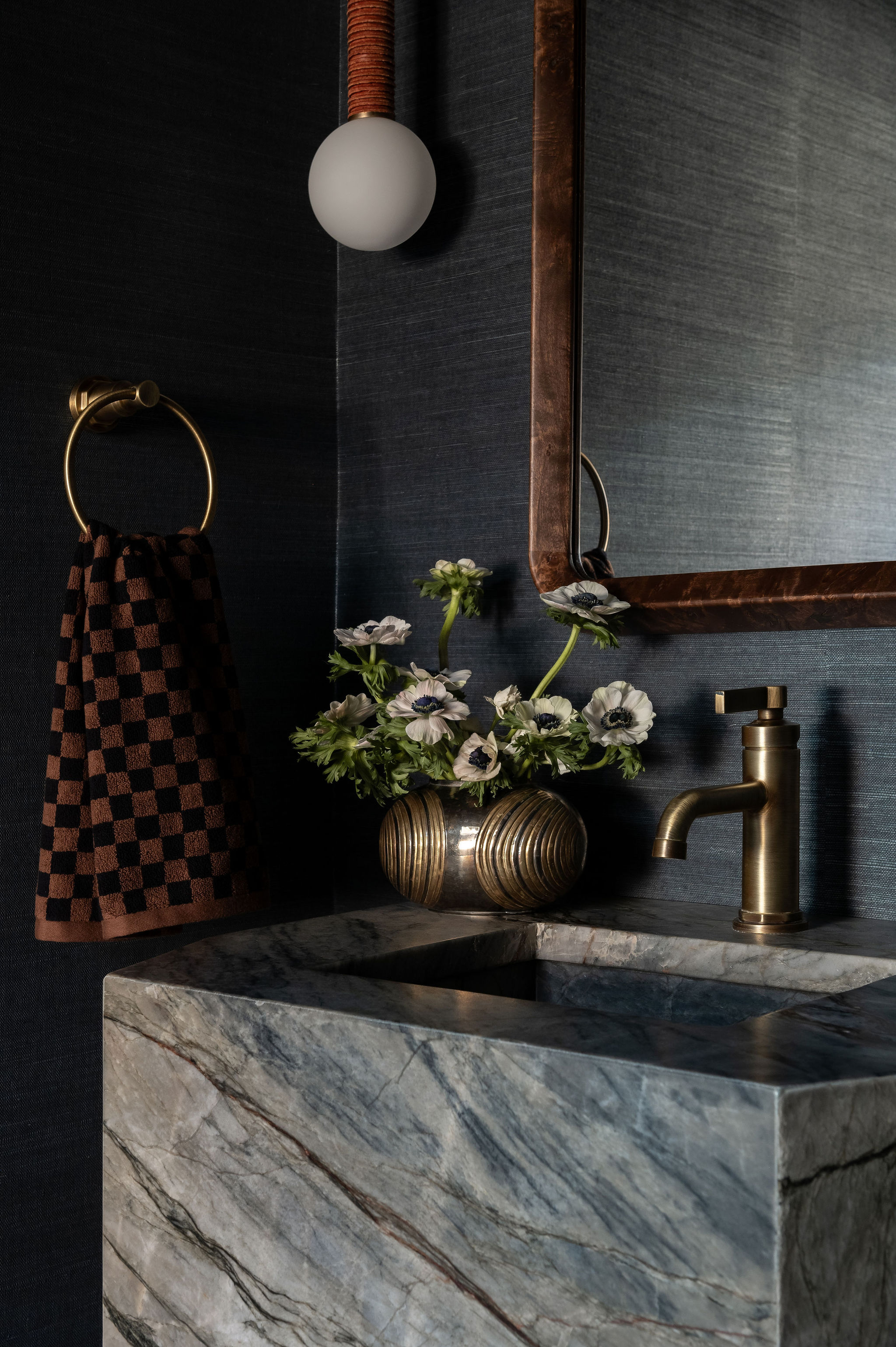 Bathroom sink with a gold faucet, a mirror, a checkered towel, and a vase of white flowers on a marble countertop.