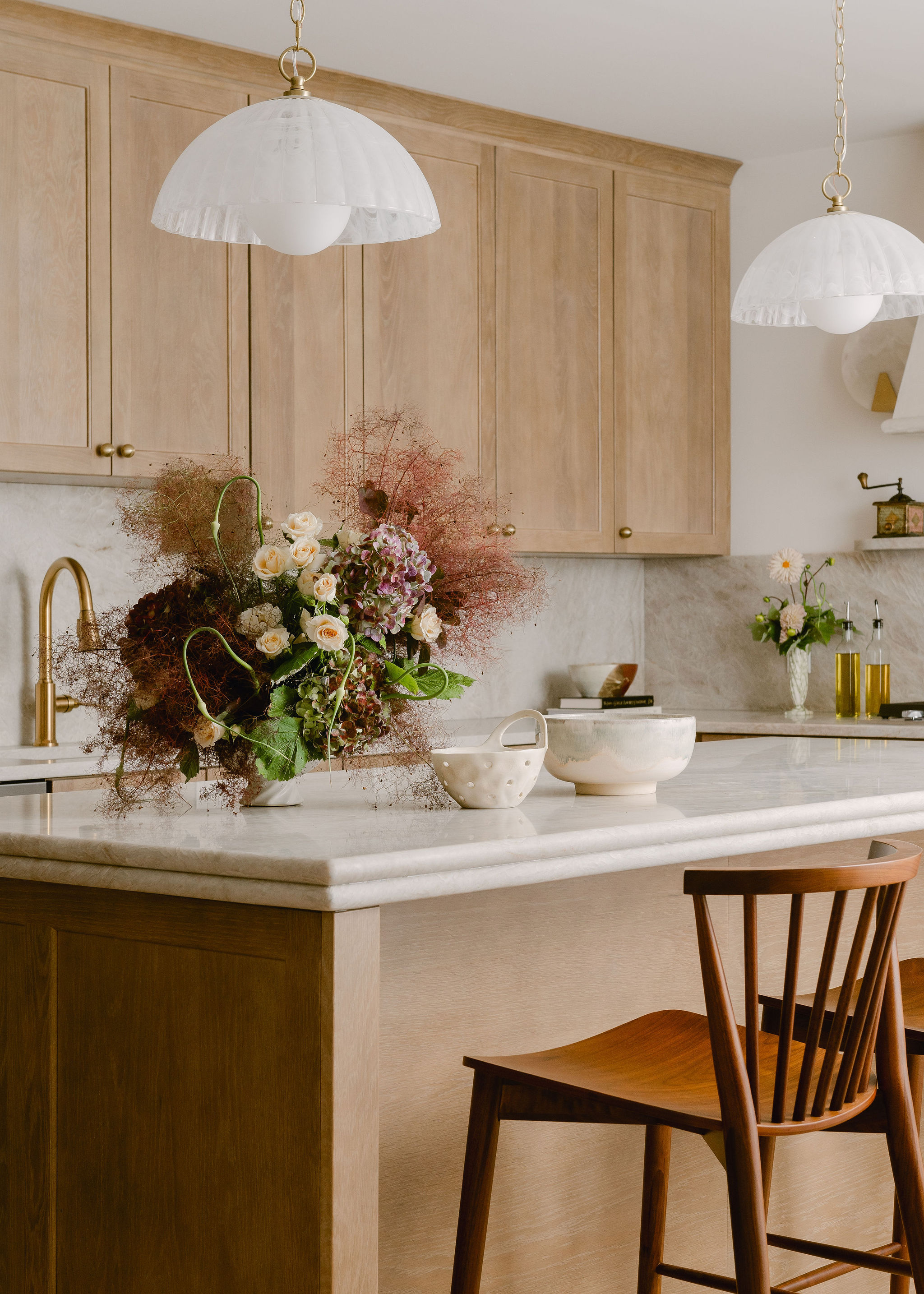 Kitchen with wooden cabinets, white marble countertop, floral arrangement, and two hanging pendant lights.