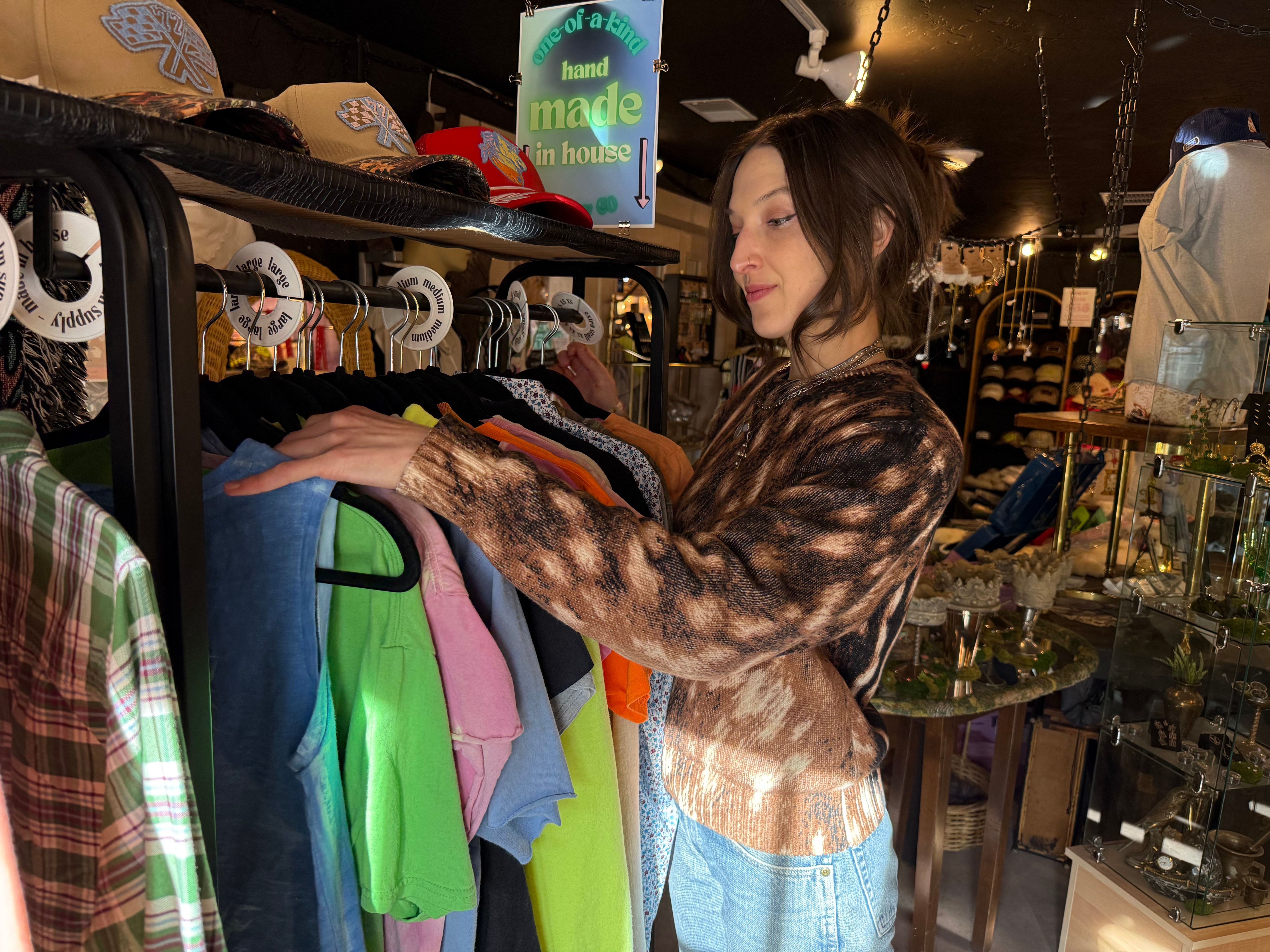 Woman browsing colorful clothes on a rack inside a store, with shelves and displays in the background.