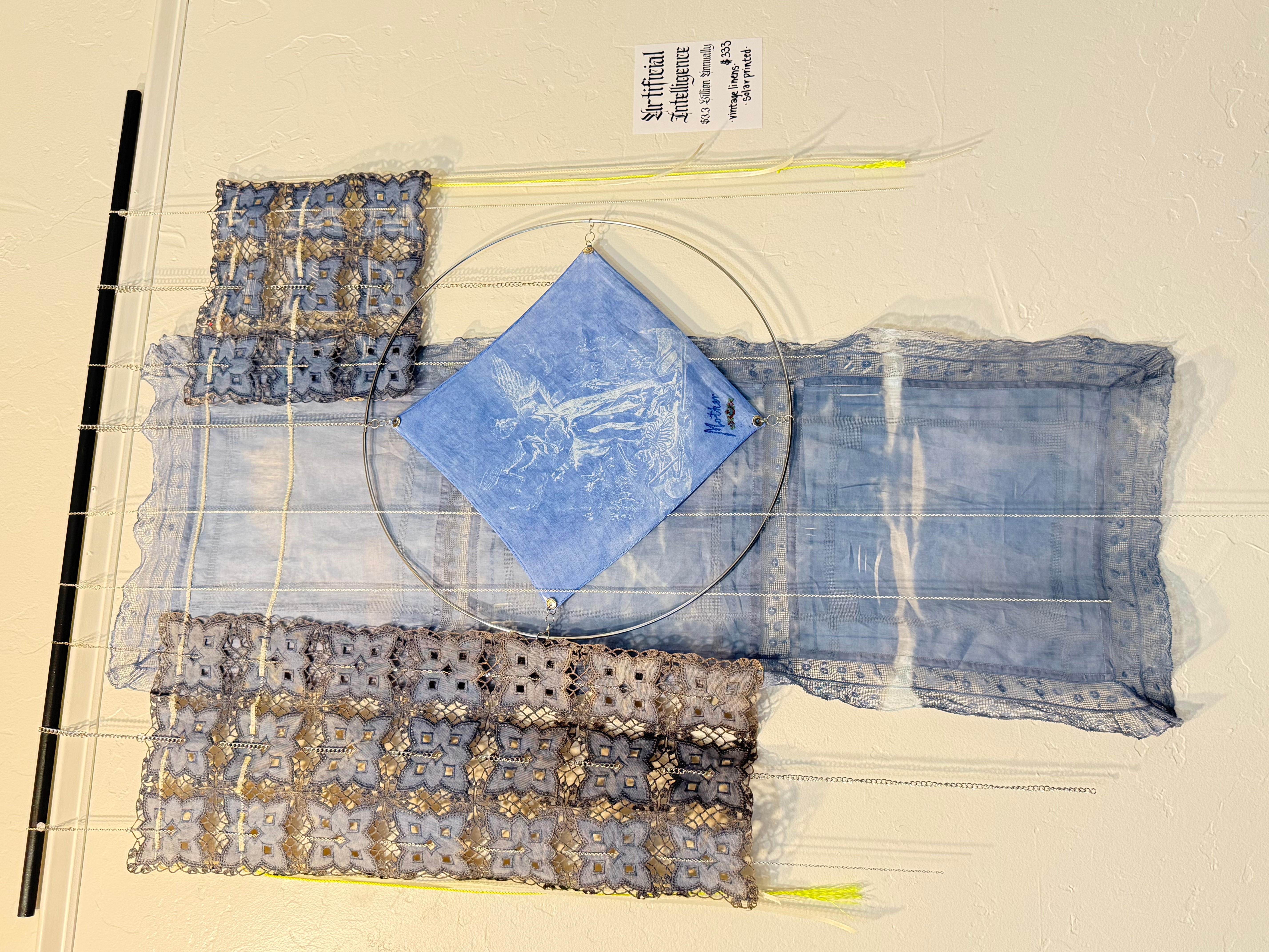 Textile art with lace, fabric, and a blue diamond-shaped piece on a white background.