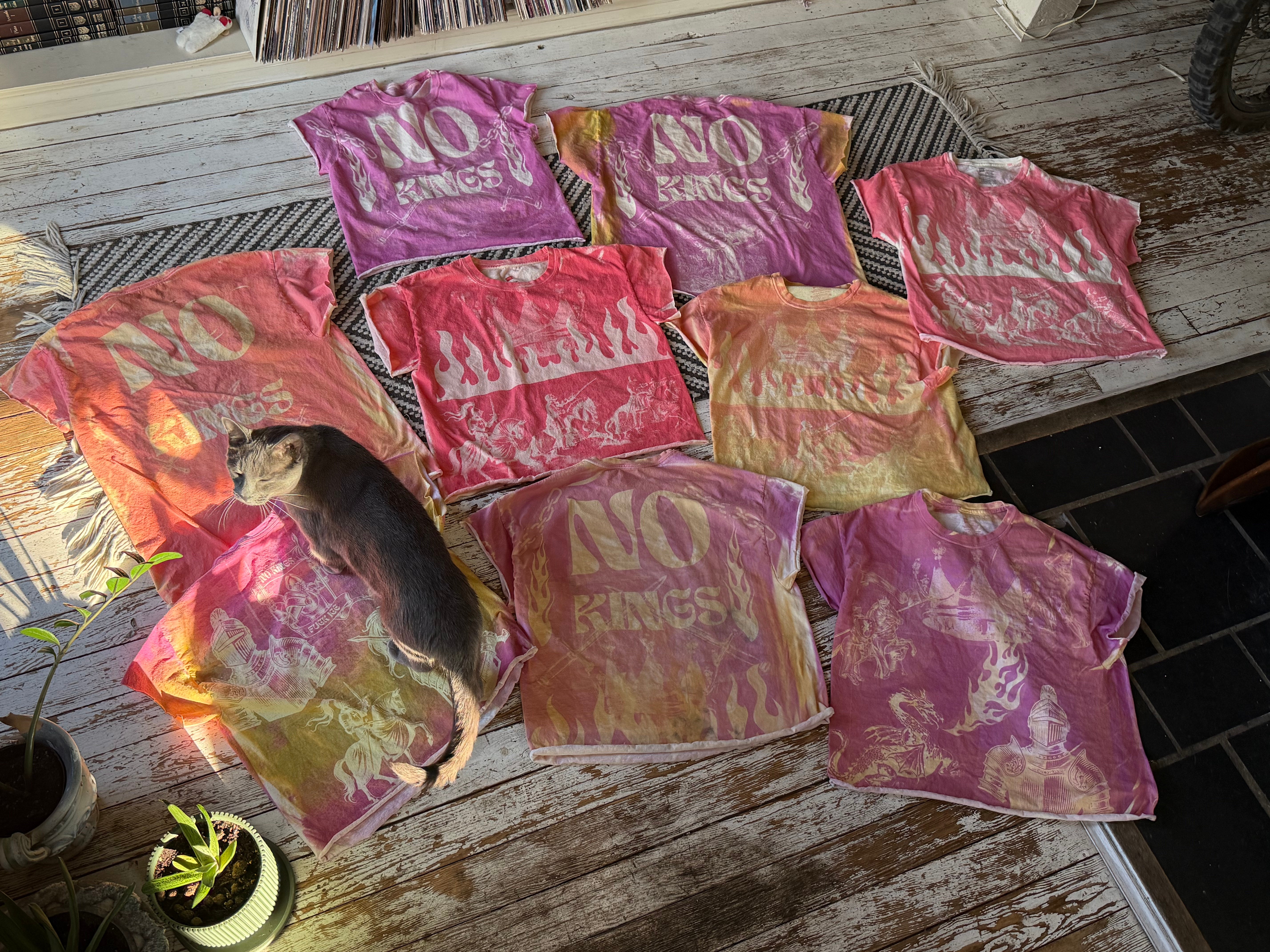 Seven colorful towels with text and a cat lying on one towel, all on a wooden surface.