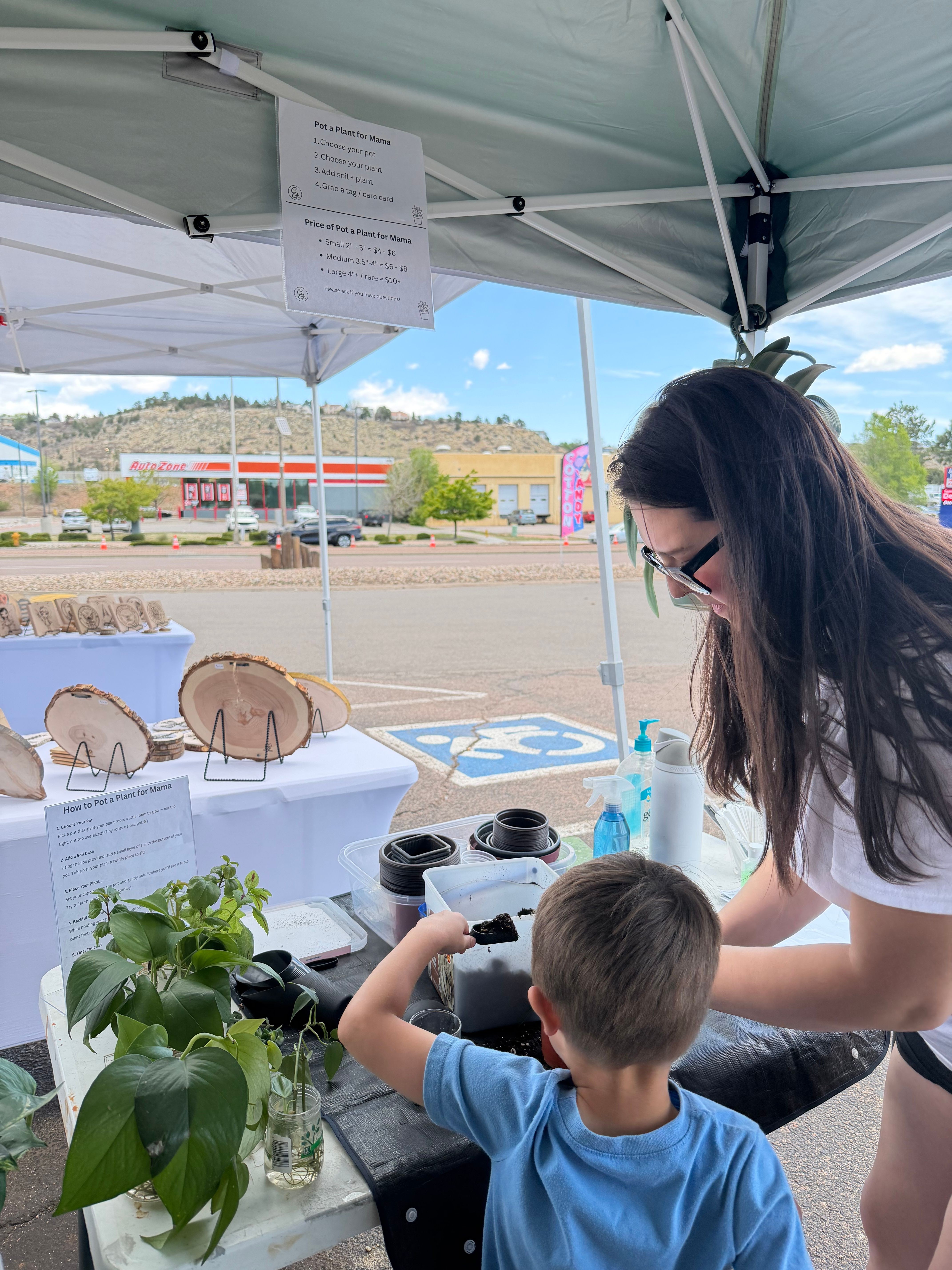 A woman and a young boy look through a microscope at an outdoor event under a tent, with a beach and buildings in background.