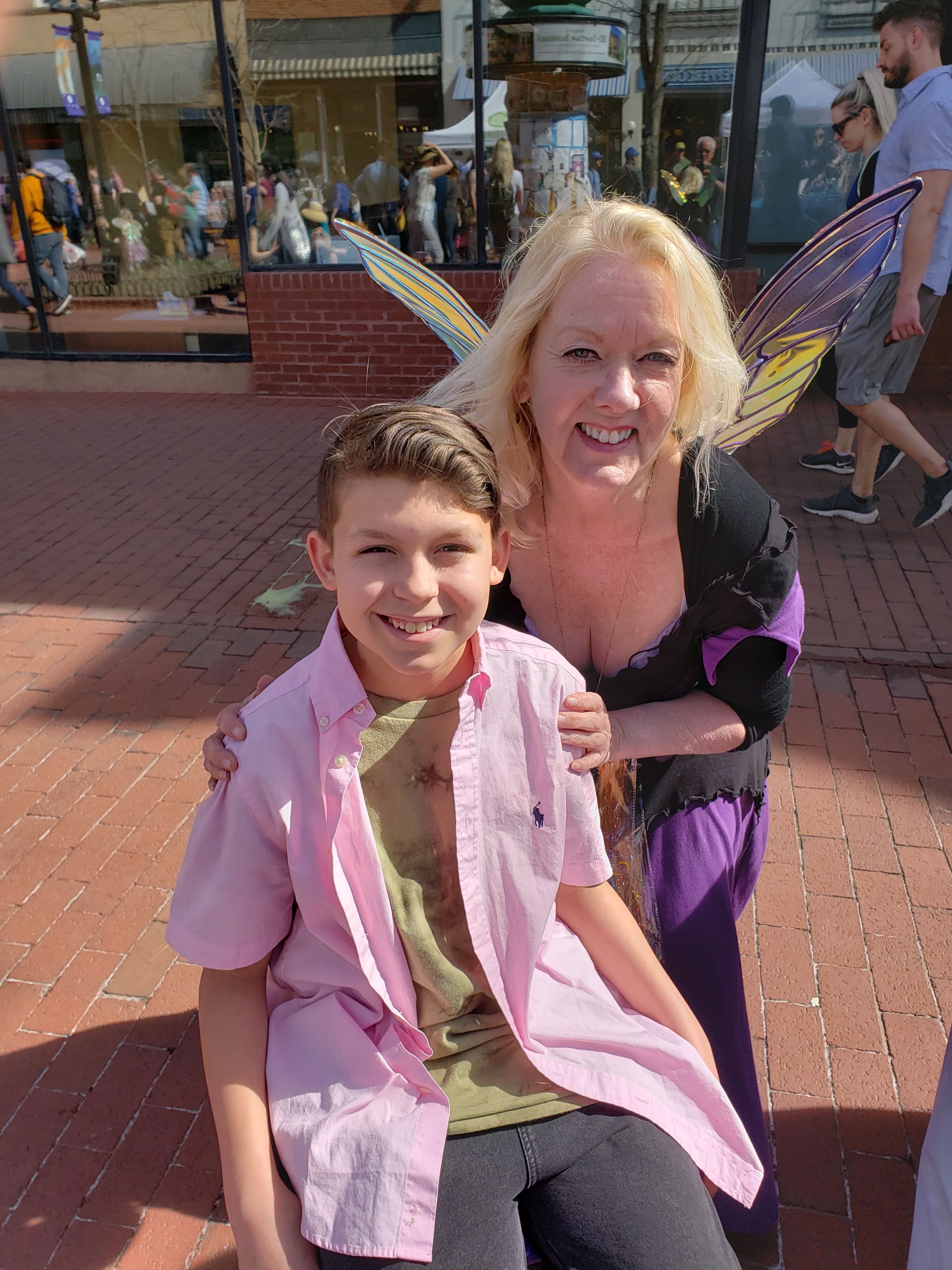 Two children, a girl with blonde hair and a boy with brown hair, smiling outdoors on a brick sidewalk.