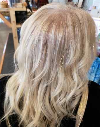 Back of a person's head with long, wavy, blonde hair in a salon setting.