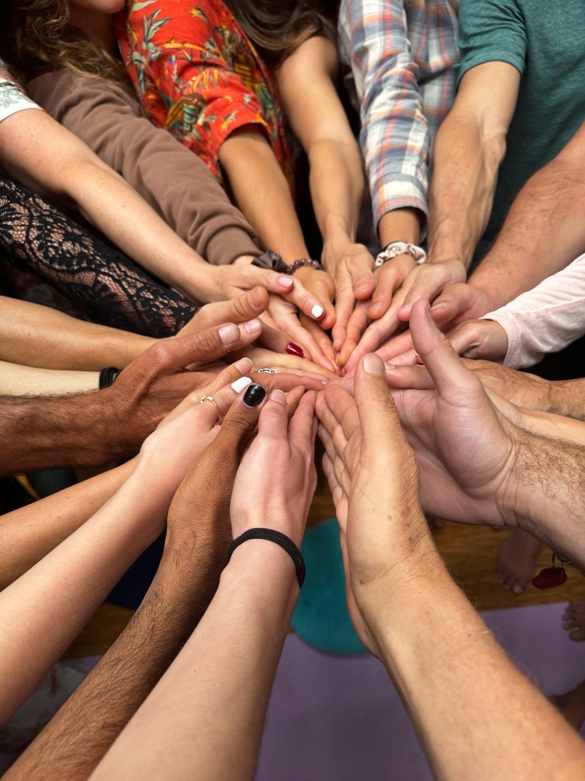 Multiple hands of diverse people join together in a circle, symbolizing unity and teamwork.