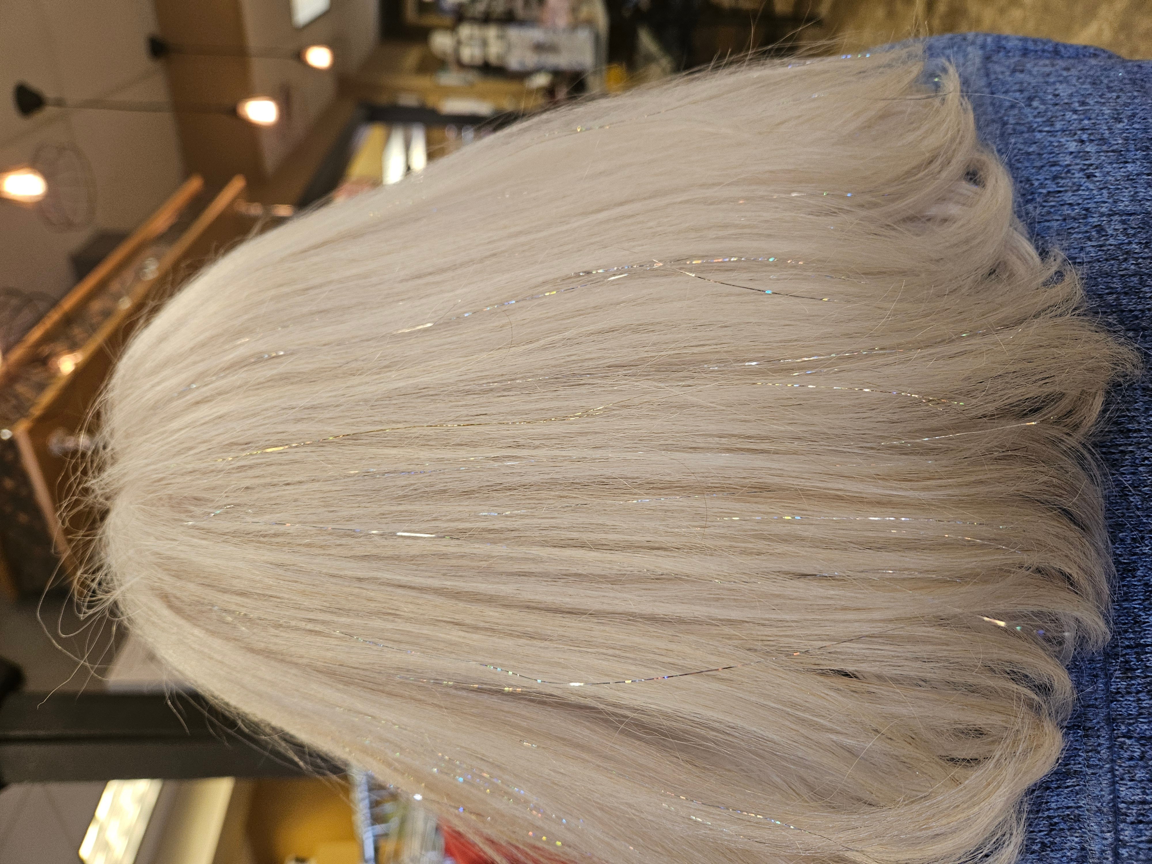 Person with straight, platinum blonde hair, wearing a blue garment, in an indoor setting with warm lighting.