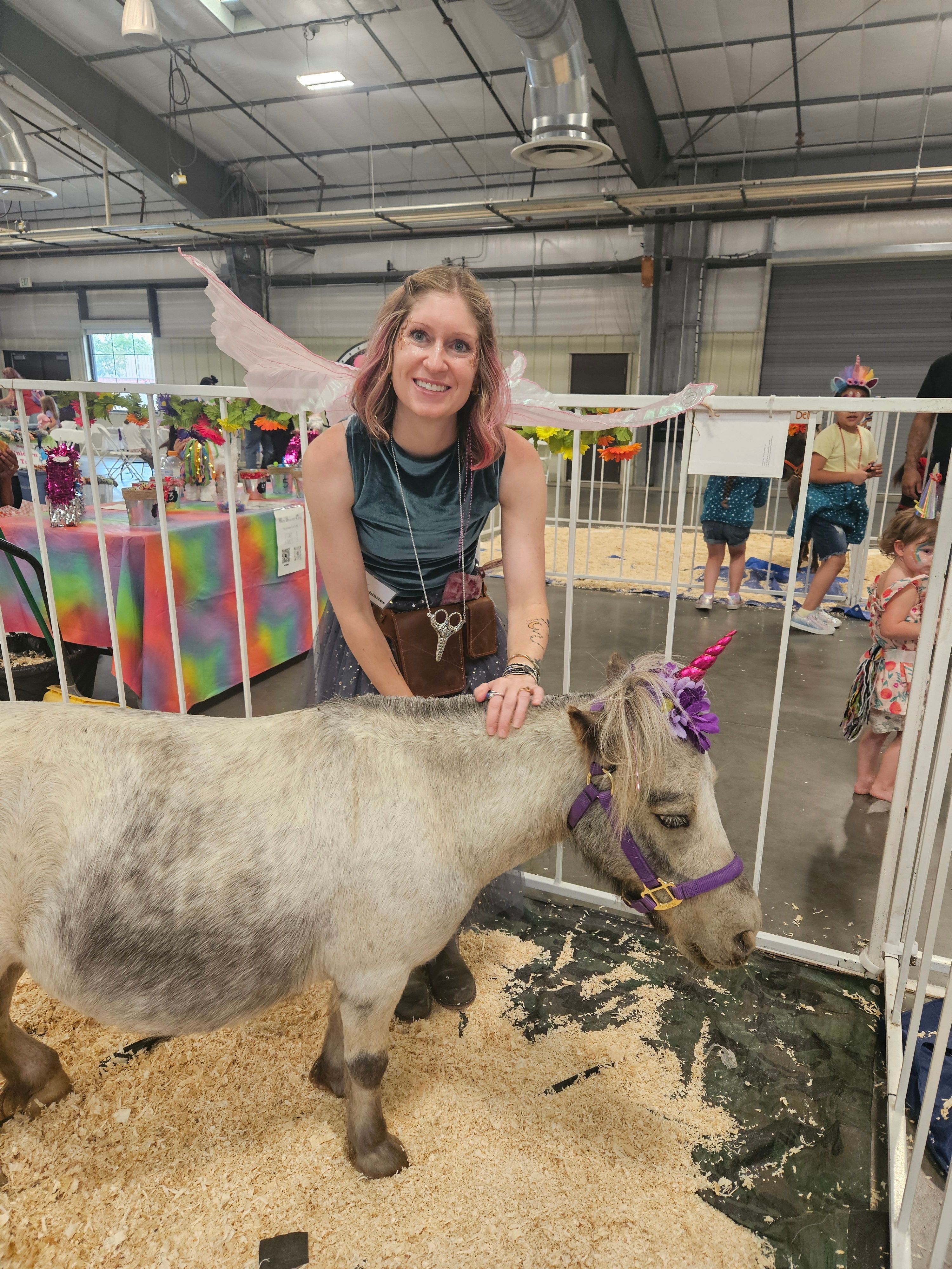 Young woman with long hair and a striped shirt interacts with a small horse in an indoor setting, colorful decorations in background.