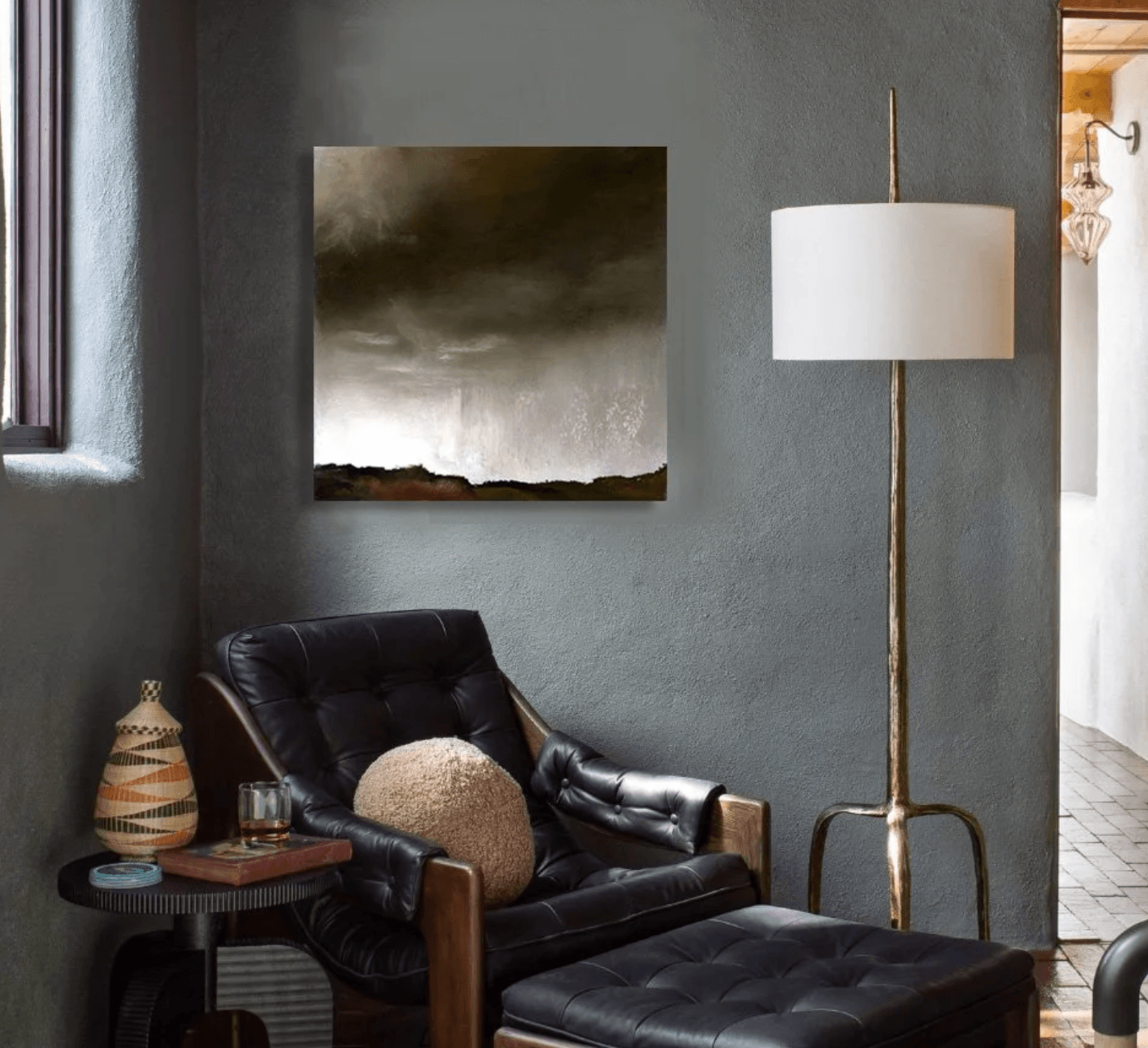 Living room corner with a black leather armchair, a floor lamp, and a painting on a gray wall.