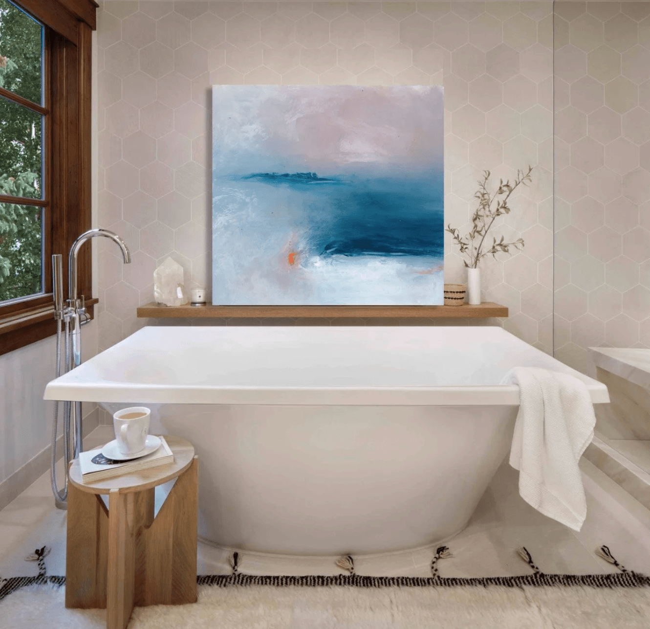 Bathtub with a white towel, a small wooden stool with a cup and saucer, and a painting above the tub.