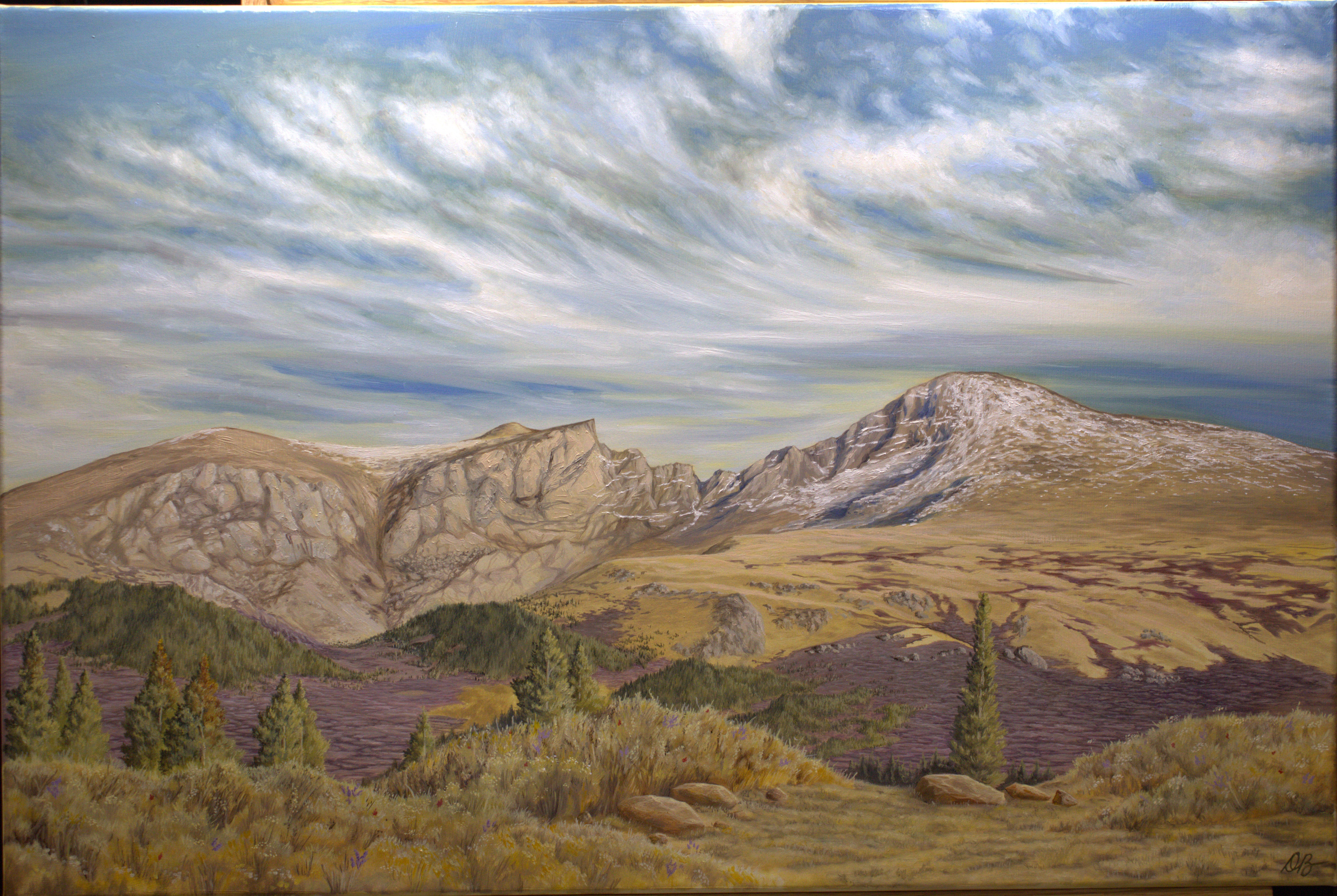 Landscape with mountains, rolling hills, trees, and a cloudy sky.