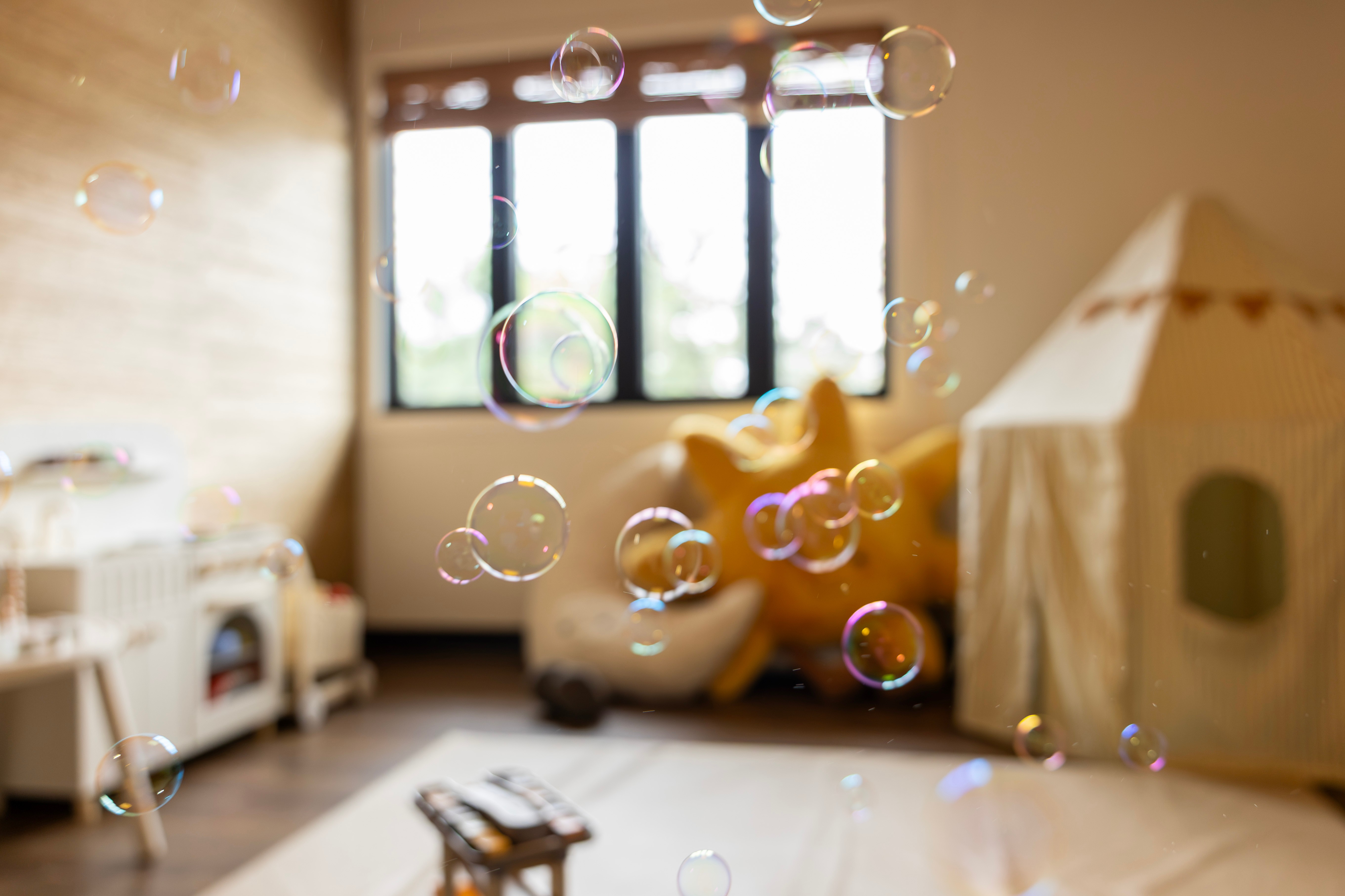 Bubbles floating in a room with a window, a yellow chair, and a play tent, with sunlight coming through the window.
