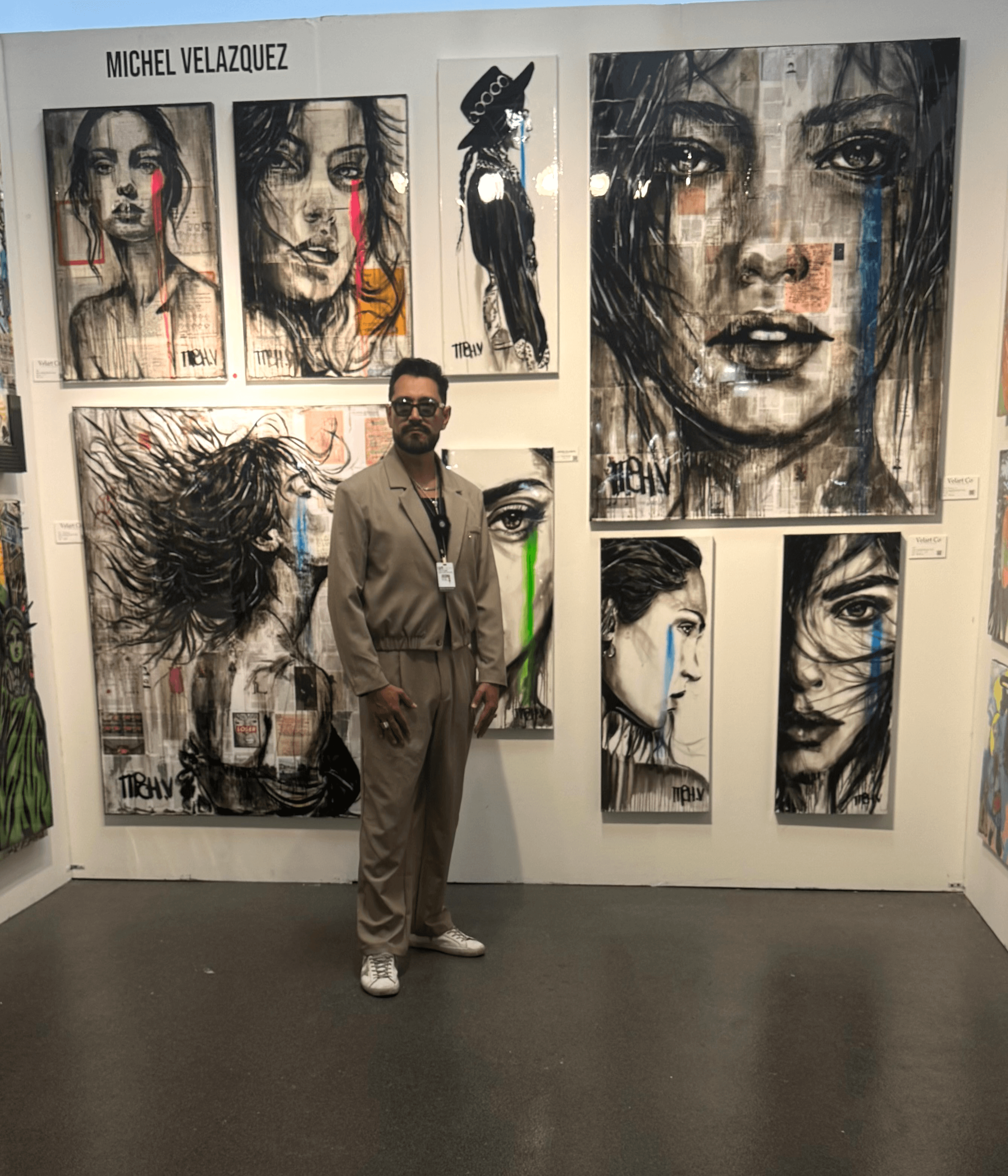Person standing in front of a wall with multiple large, expressive portrait paintings, including a woman with tears and a woman with colorful streaks.