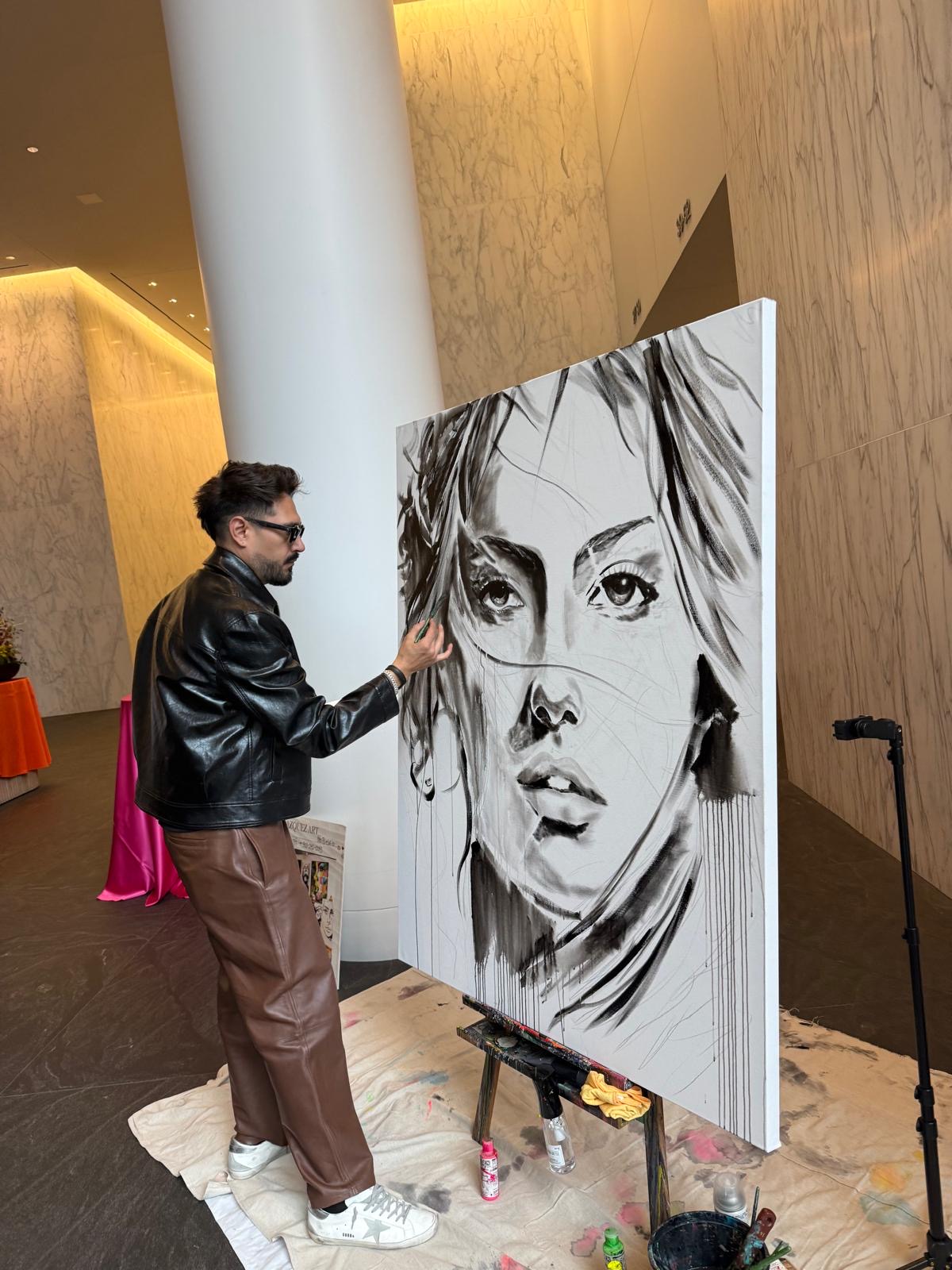 Person in black jacket and brown pants drawing a large black and white portrait on an easel.